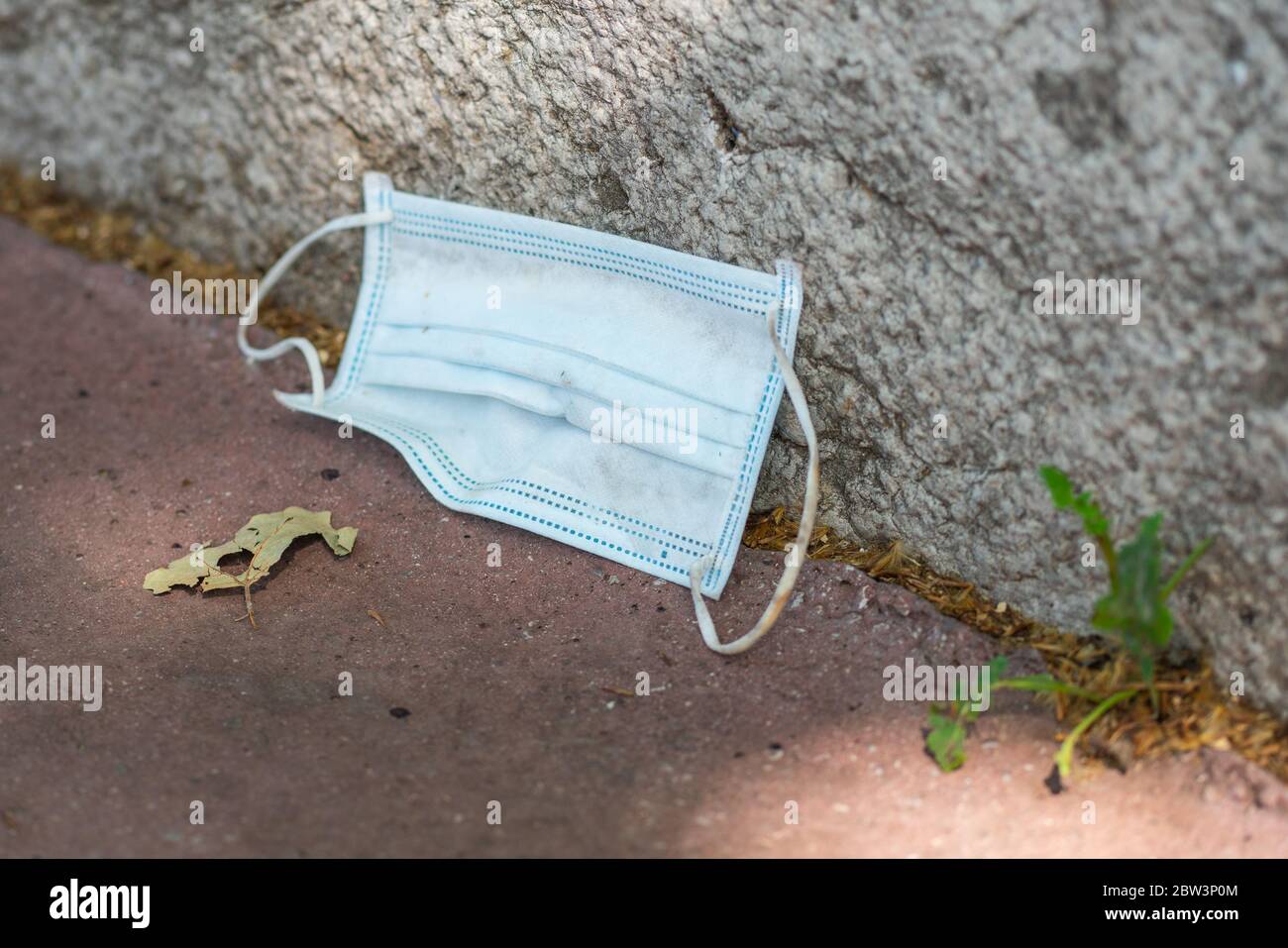 Maschera chirurgica scartata o maschera facciale abbandonata a terra in strada Foto Stock