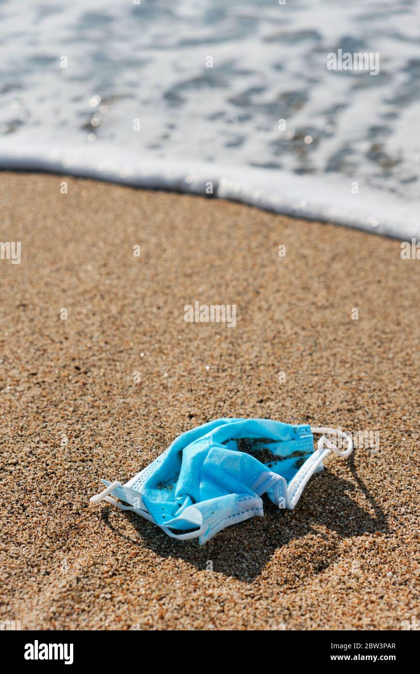 primo piano di una maschera chirurgica blu usata gettata sulla sabbia bagnata della riva di una spiaggia Foto Stock