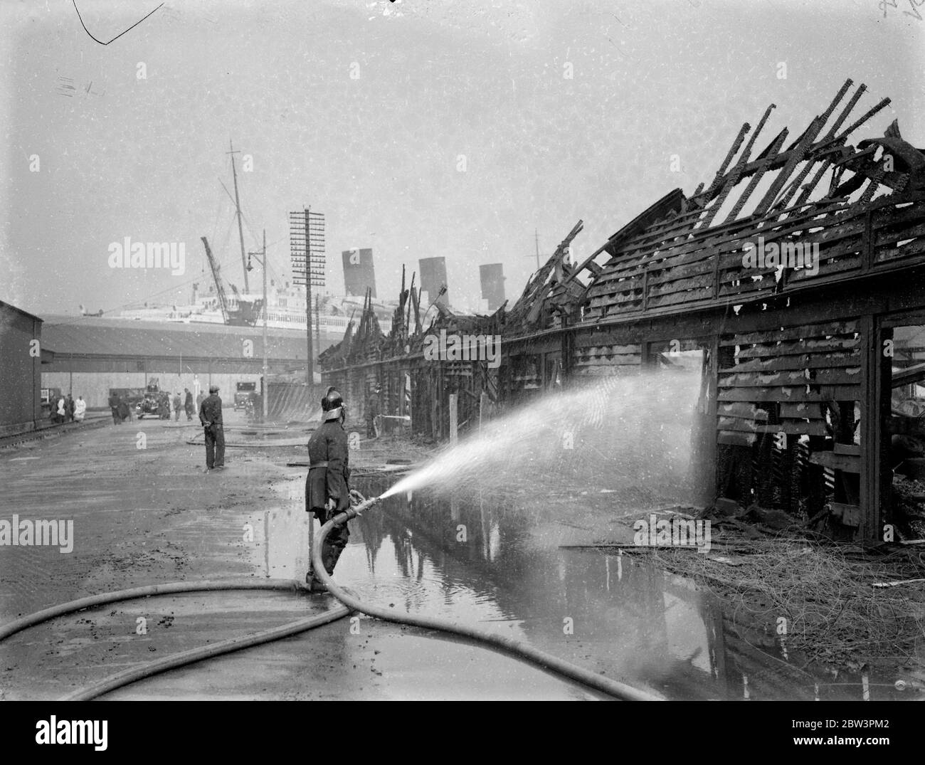 I negozi e gli uffici di Southampton sono distrutti da un incendio. Adiacente alla residenza della Regina Maria. Gli uffici e i negozi della Royal Mail Steamship Company presso i moli di Southampton sono stati completamente distrutti da un incendio scoppiato oggi ( domenica ) . Gli edifici sono vicini alla banca in cui la collinetta gigante ' Queen Mary ' è in preparazione per il suo viaggio inaugurale . Spettacoli fotografici, vigili del fuoco al lavoro sulle rovine bruciate a Southampton , sullo sfondo è la ' Queen Mary ' . 3 maggio 1936 . Foto Stock