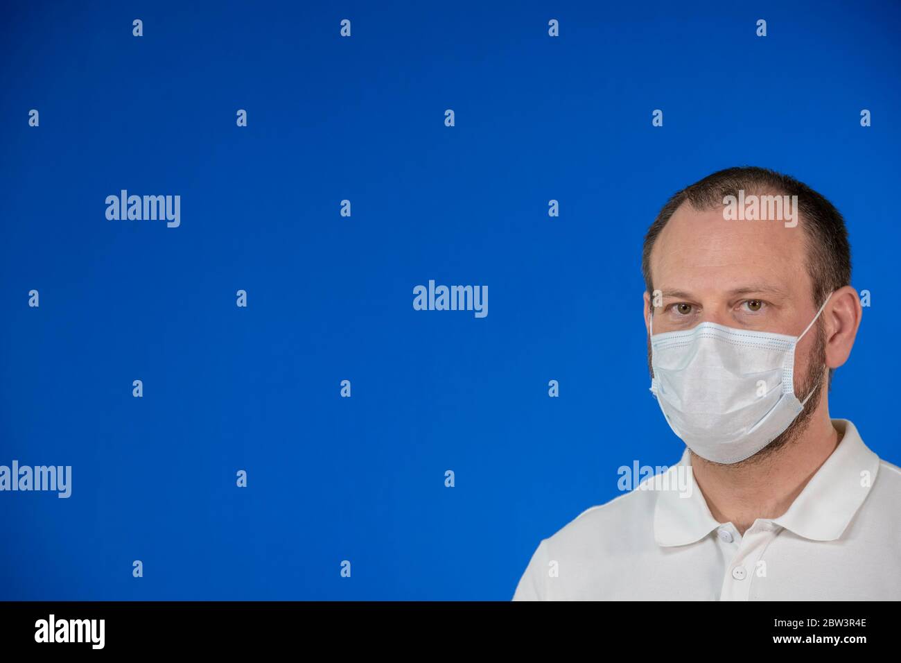 Uomo isolato indossando maschera protettiva su sfondo blu e con ampio spazio per la copia. Concetto di problema di salute, misura preventiva contro Coronavirus Foto Stock