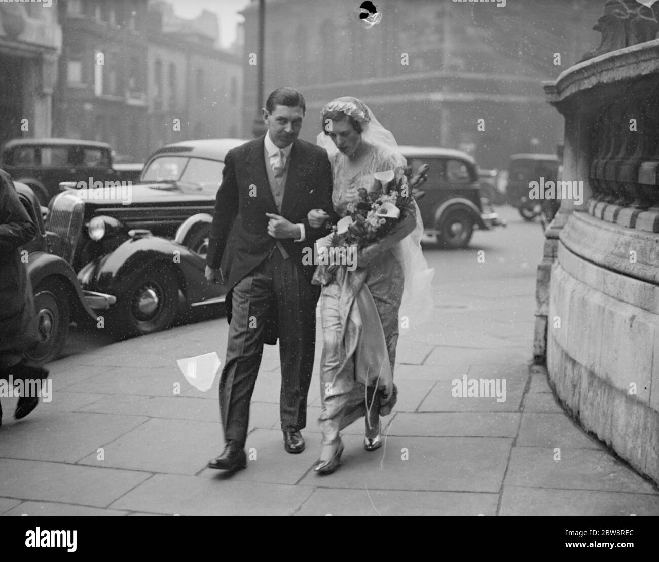 Processione nuziale attraverso Langham luogo dopo tutte le anime matrimonio . Dopo il loro matrimonio alla Chiesa di All Souls , Langham Place , W , capitale Victor Paley della brigata del fucile , e la sua sposa , forma Miss Susan Paine , camminarono per la strada con il loro retinue al Langham Hotel , dove si svolse la reception . Spettacoli fotografici , la processione nuziale che attraversa la strada le accanto allo sposo e sposa . 14 aprile 1936 Foto Stock