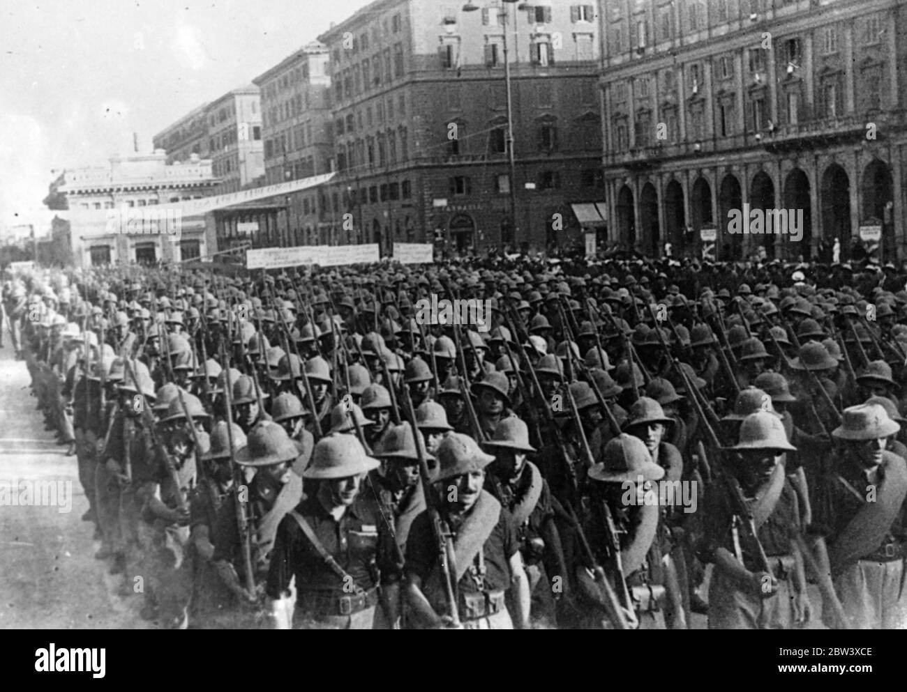 Mussolini accoglie le truppe che ritornano dal servizio abissino . Alzato a mano in saluto , il Signore Mussolini accolse un grande distacco di sole - aiutò le truppe italiane mentre marciavano con le attrezzature complete attraverso Piazza Venezia a Roma al loro ritorno dal servizio in Abissinia . Grandi folle si sono radunate nelle strade per salutare i battaglioni di ritorno . Spettacoli fotografici : truppe italiane , che indossano il sole - caschi e attrezzature complete , che marciano attraverso Piazza Venezia a Roma al loro ritorno da Addis Abeba . 11 settembre 1936 Foto Stock
