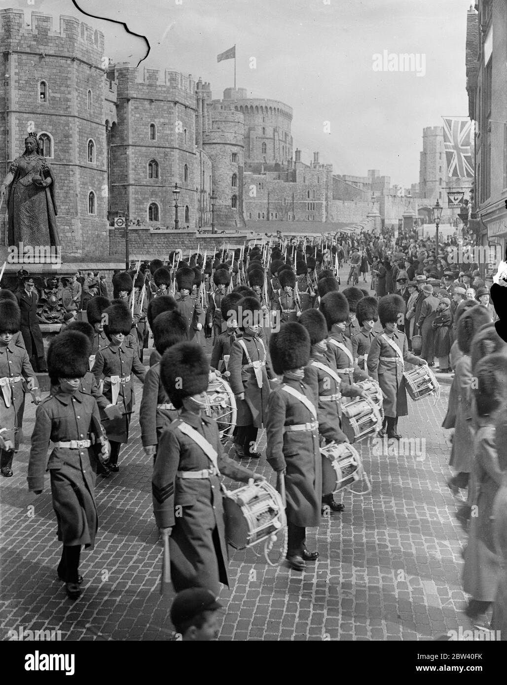 Ora che il Re e la Regina hanno preso la residenza al Castello di Windsor, una guardia completa è stata montata per la prima volta da quando il Re Giorgio V li ultimi giorni. Spettacoli fotografici: La guardia, guidata dalla band, si allontana dal Castello di Windsor dopo il cambio della guardia. 9 aprile 1937 Foto Stock