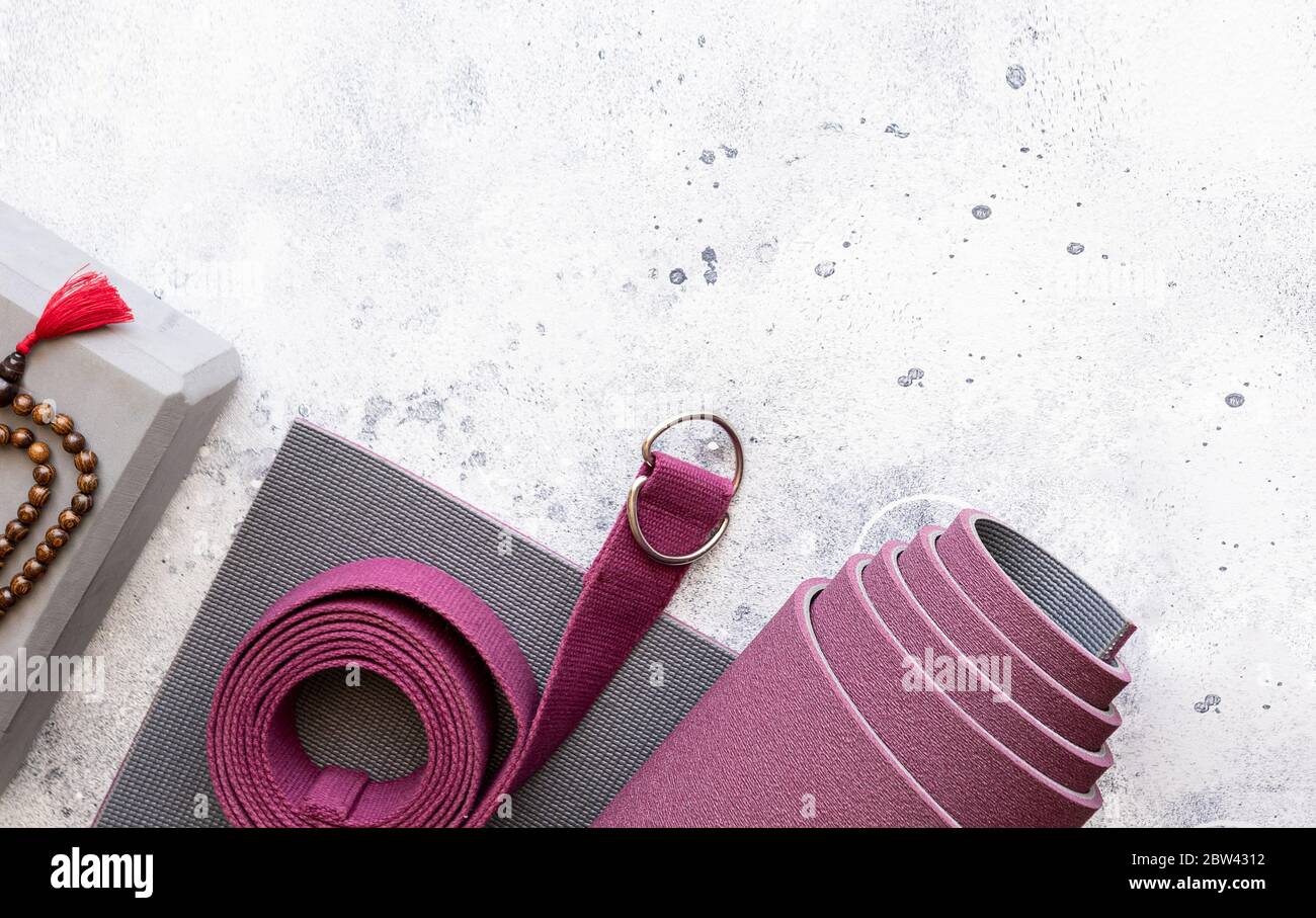 Accessori per yoga. Tappeto per esercizi arrotolati, perline di legno mala, blocchi yoga e cintura su fondo grigio in cemento. Yogi è un'attività di sostegno essenziale per la pratica e per il m. Foto Stock