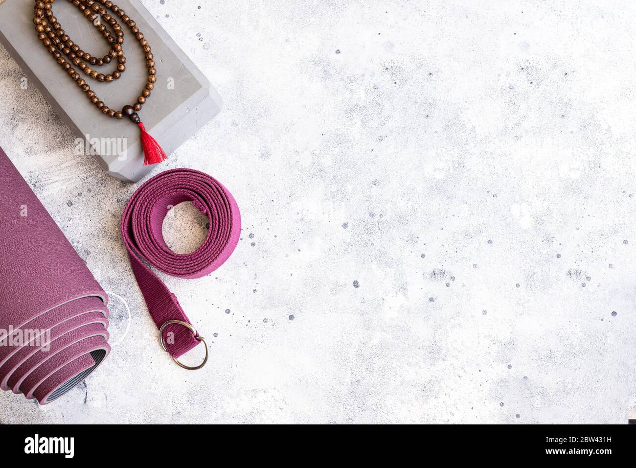 Accessori per yoga. Tappeto per esercizi arrotolati, perline di legno mala, blocchi yoga e cintura su fondo grigio in cemento. Yogi è un'attività di sostegno essenziale per la pratica e per il m. Foto Stock