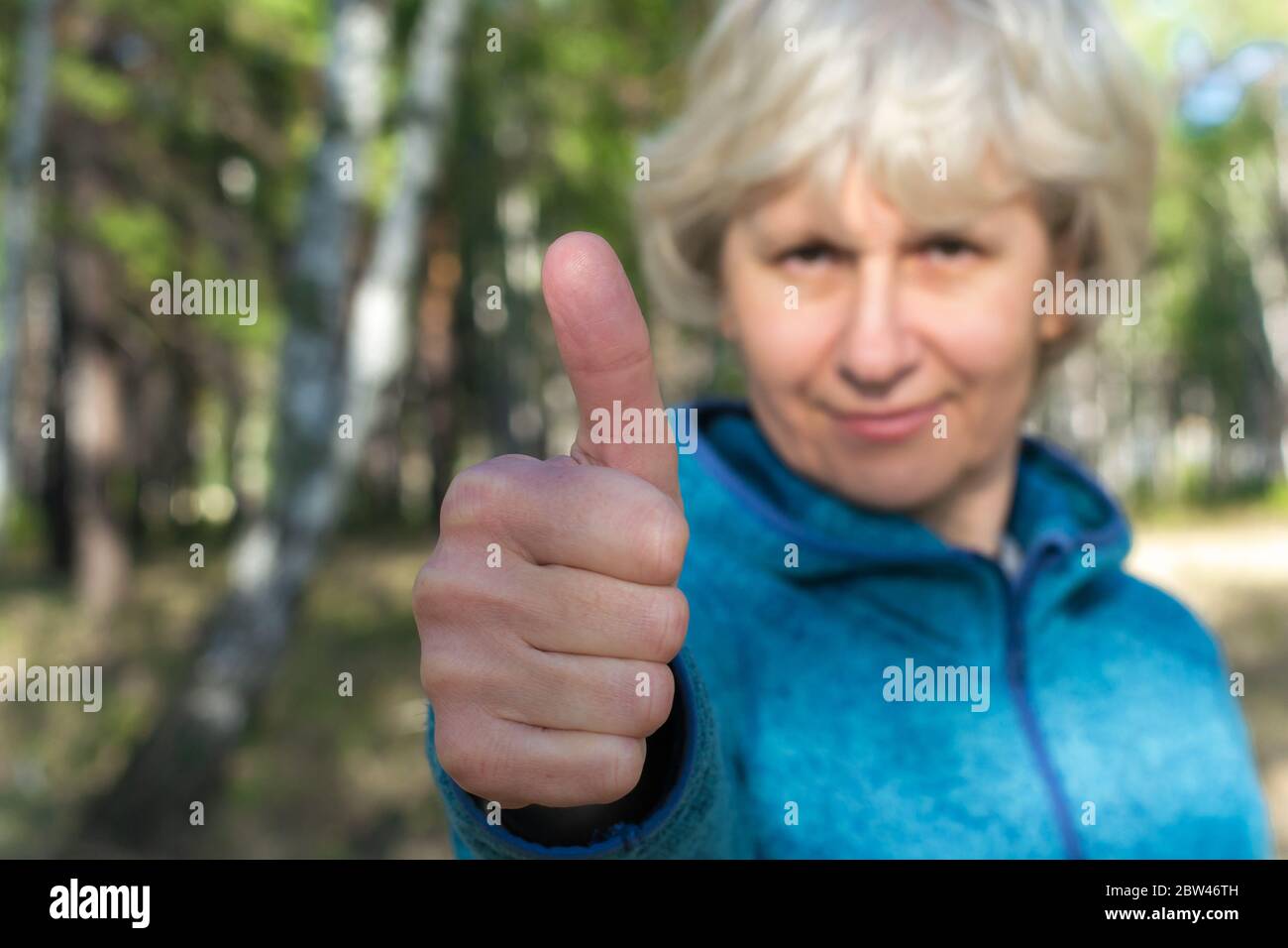 Una donna di mezza età sorride e mostra un pollice in su. Passeggiate nel parco in una giornata di sole. Buon umore. Foto Stock