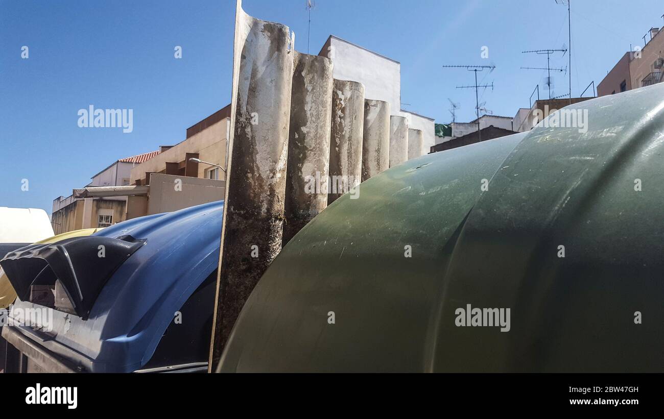 Fogli corrugati di cemento di fibra gettati fra le lattine di cestino. Gestione errata del concetto di rifiuti pericolosi Foto Stock