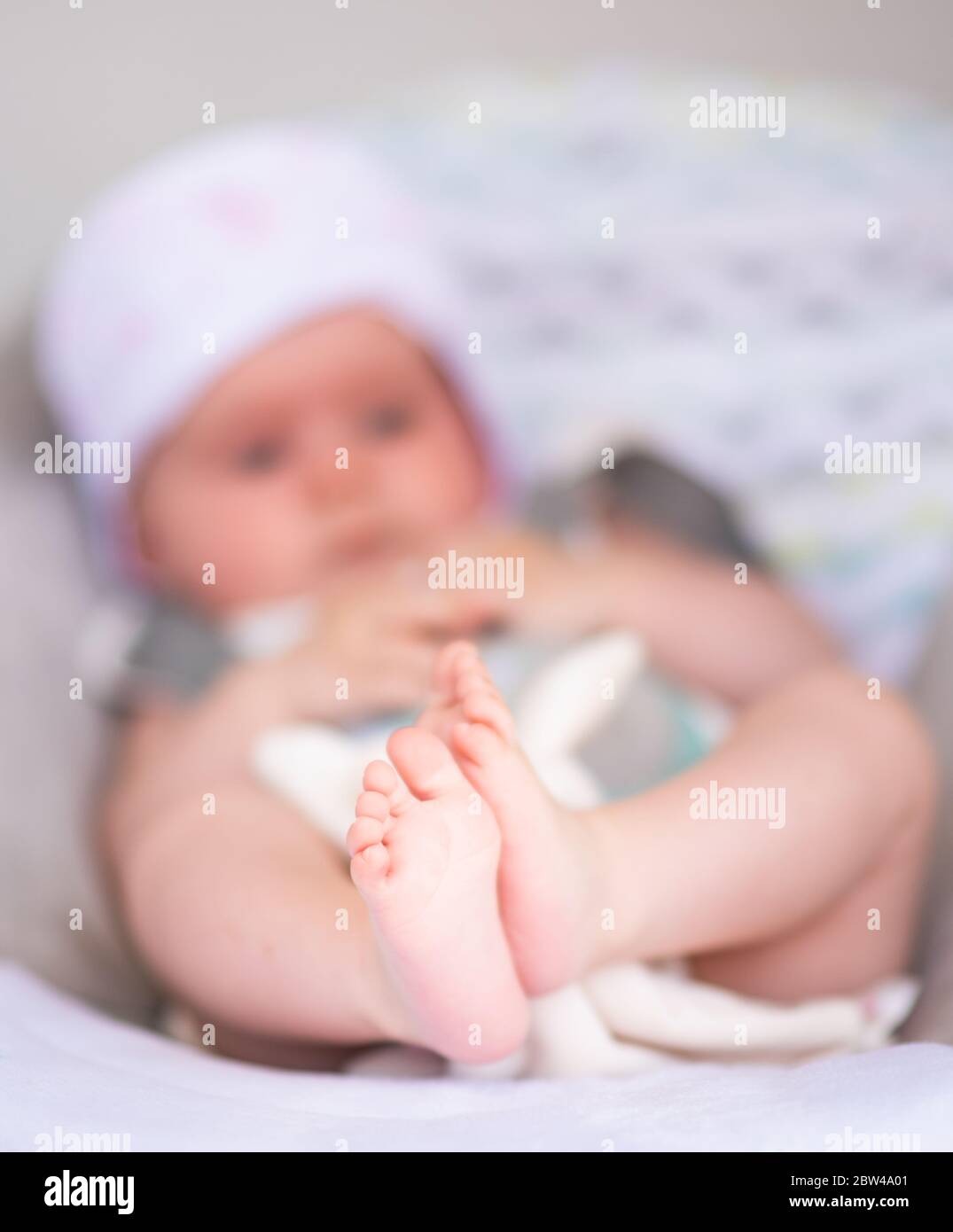 Primo piano di bambina dolce di 6 mesi in altalena elettrica o culla all'aperto nella soleggiata giornata estiva. Primo piano di piedi piccoli Foto Stock