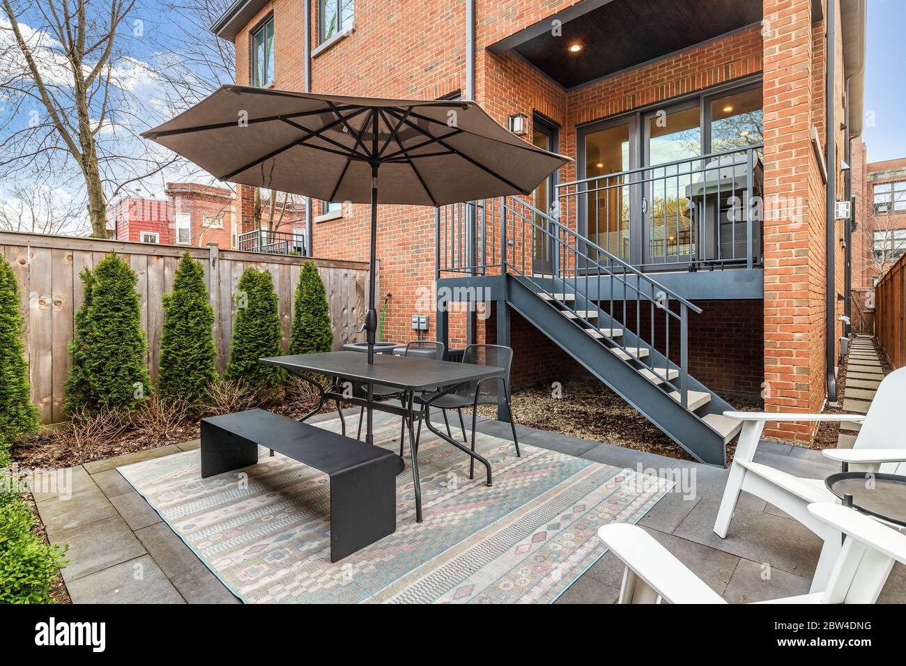 Un piccolo patio recintato sul retro di un duplex del centro di Chicago con un tavolo da picnic e un ombrello circondati da sedie bianche. Foto Stock