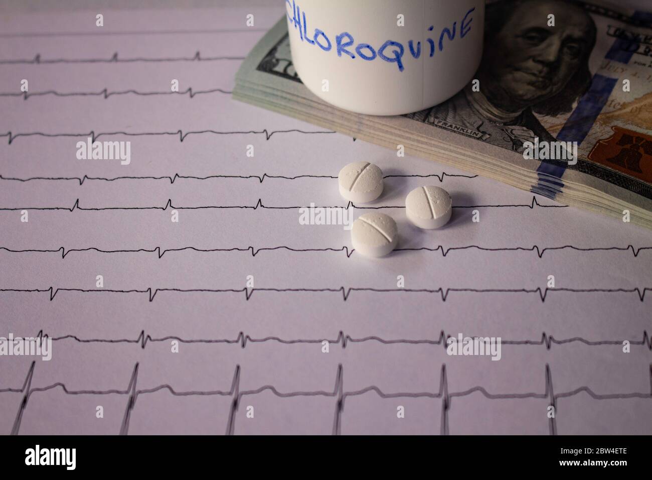 Pillole su un elettrocardiogramma. Cento dollari di bollette su un EKG. Contenitore bianco con 'idrossiclorochina' scritto sul lato. Concetto di costo elevato di Foto Stock