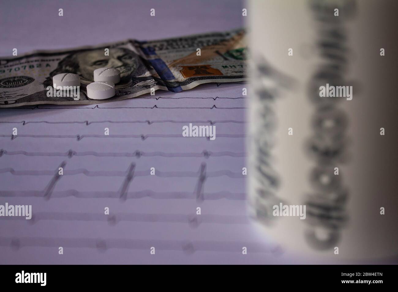 Pillole su un elettrocardiogramma. Cento dollari di bollette su un EKG. Contenitore bianco con 'idrossiclorochina' scritto sul lato. Concetto di costo elevato di Foto Stock
