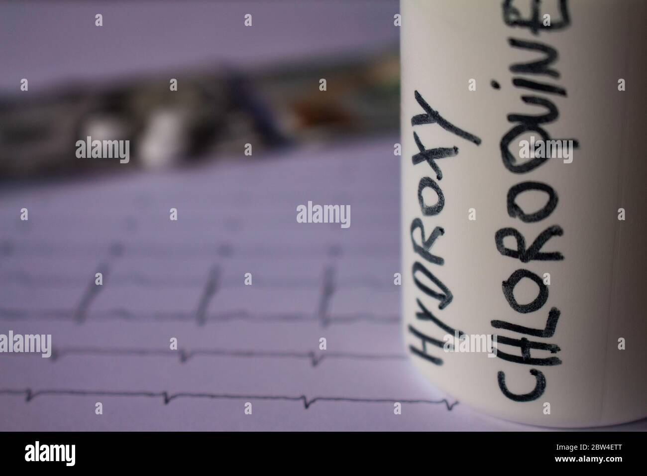 Pillole su un elettrocardiogramma. Cento dollari di bollette su un EKG. Contenitore bianco con 'idrossiclorochina' scritto sul lato. Concetto di costo elevato di Foto Stock