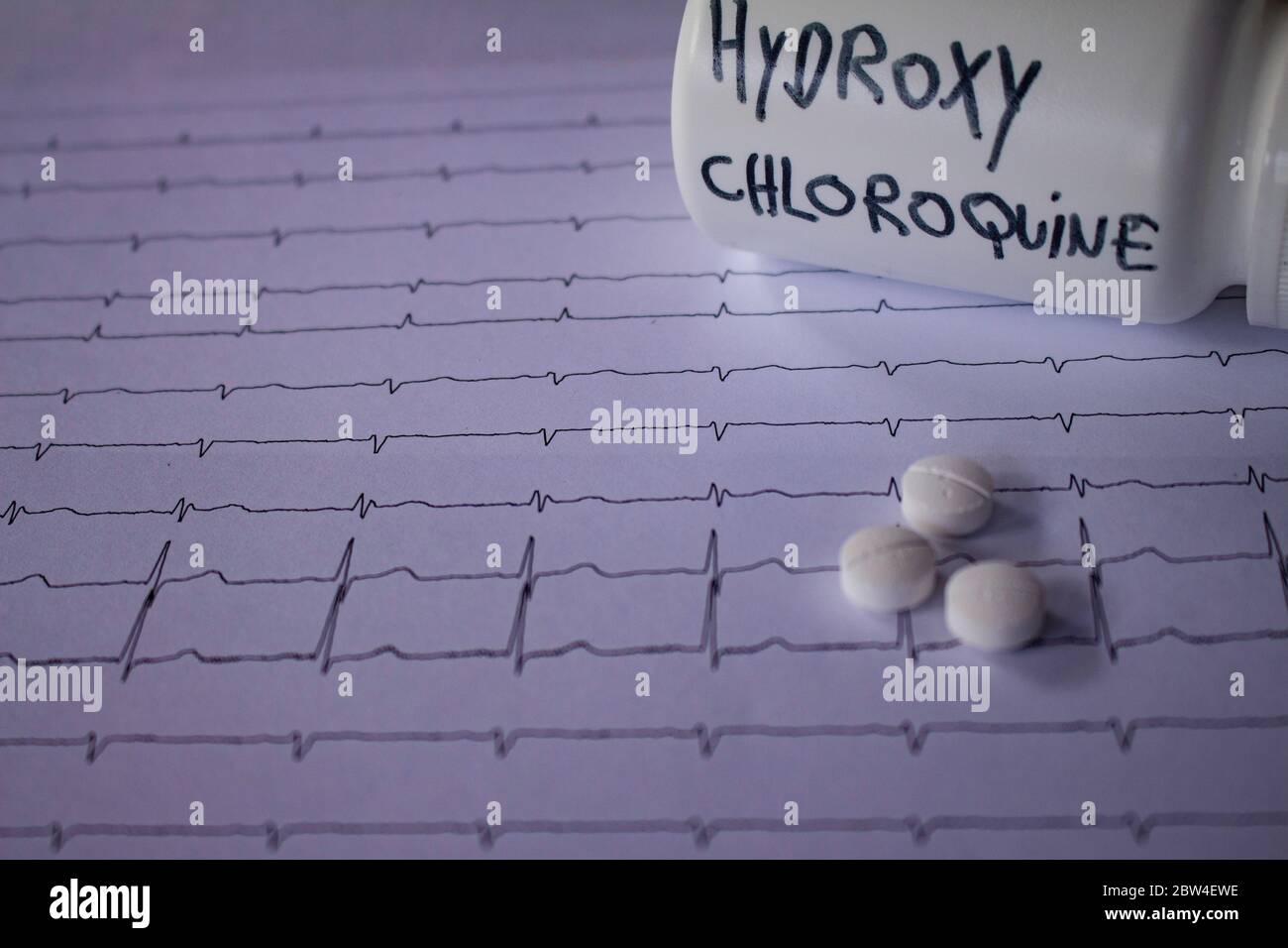 Effetti avversi sul cuore da parte di idrossiclorochina o clorochina. Pillole su un elettrocardiogramma. Contenitore bianco con scritta 'idrossiclorochina' Foto Stock