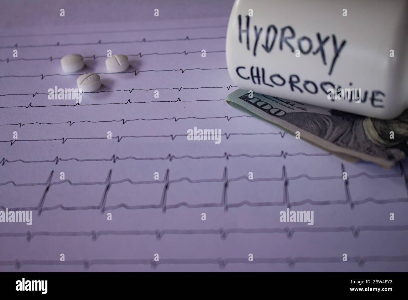 Pillole su un elettrocardiogramma. Cento dollari di bollette su un EKG. Contenitore bianco con 'idrossiclorochina' scritto sul lato. Concetto di costo elevato di Foto Stock