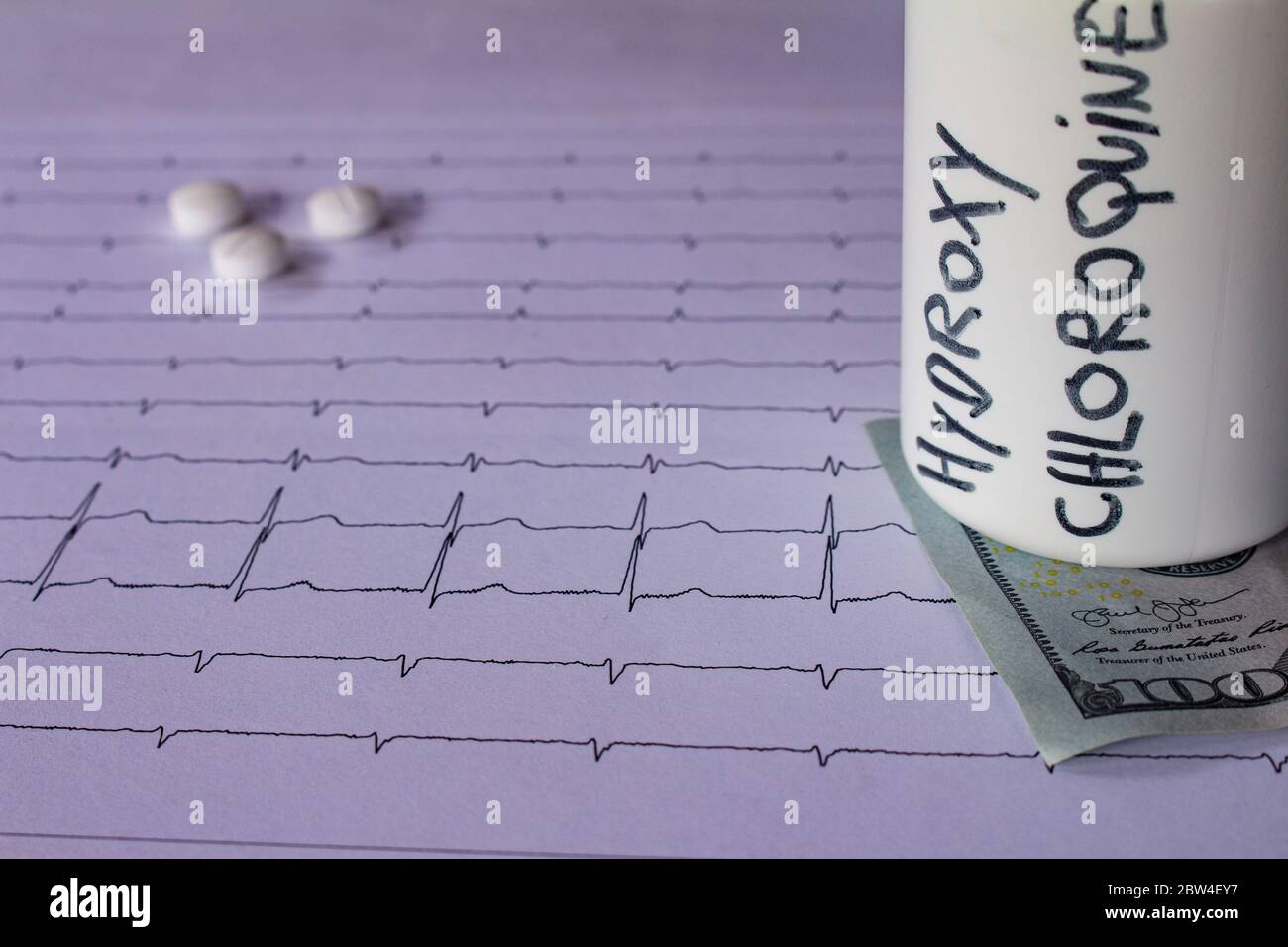 Pillole su un elettrocardiogramma. Cento dollari di bollette su un EKG. Contenitore bianco con 'idrossiclorochina' scritto sul lato. Concetto di costo elevato di Foto Stock