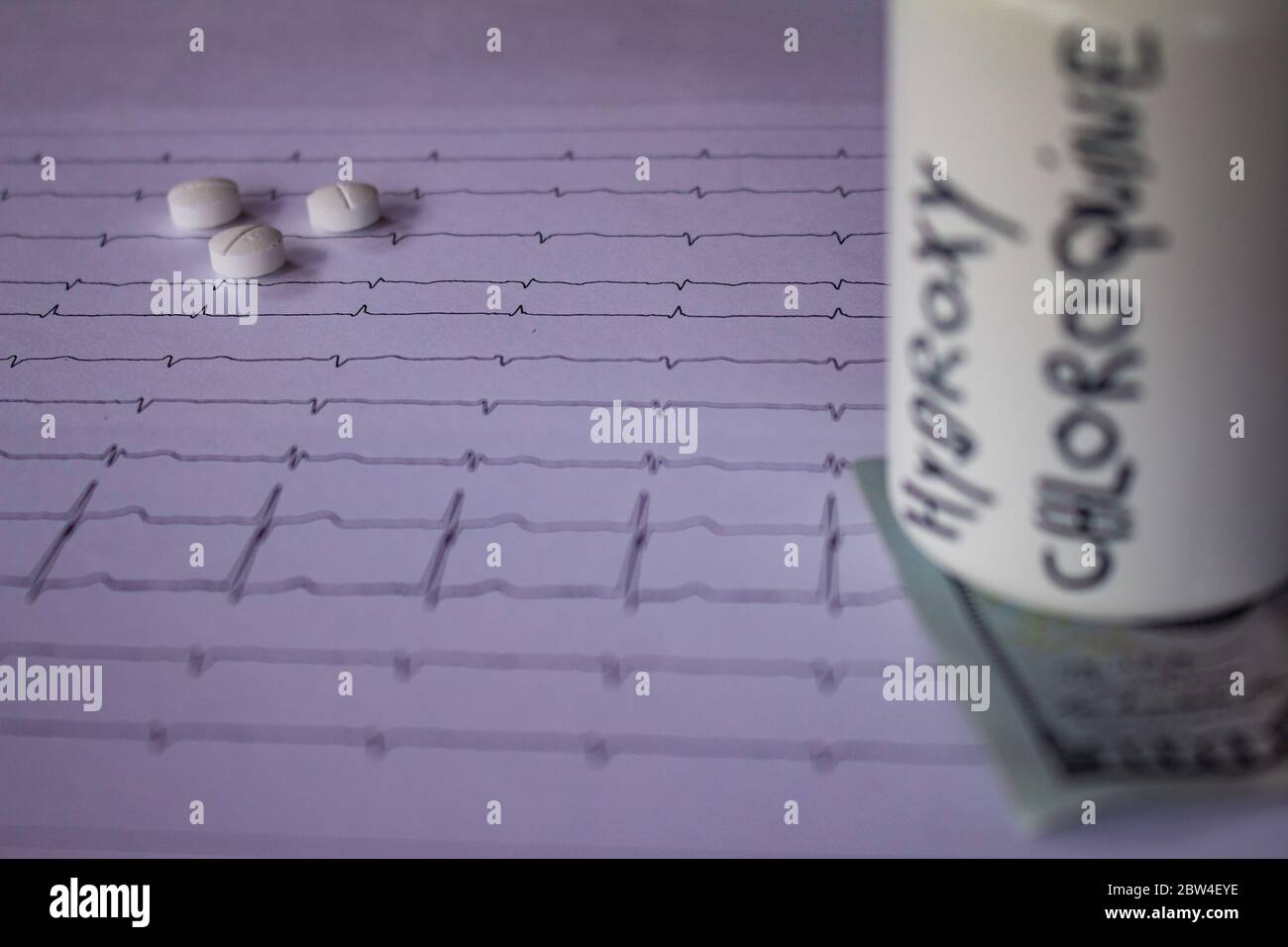 Pillole su un elettrocardiogramma. Cento dollari di bollette su un EKG. Contenitore bianco con 'idrossiclorochina' scritto sul lato. Concetto di costo elevato di Foto Stock