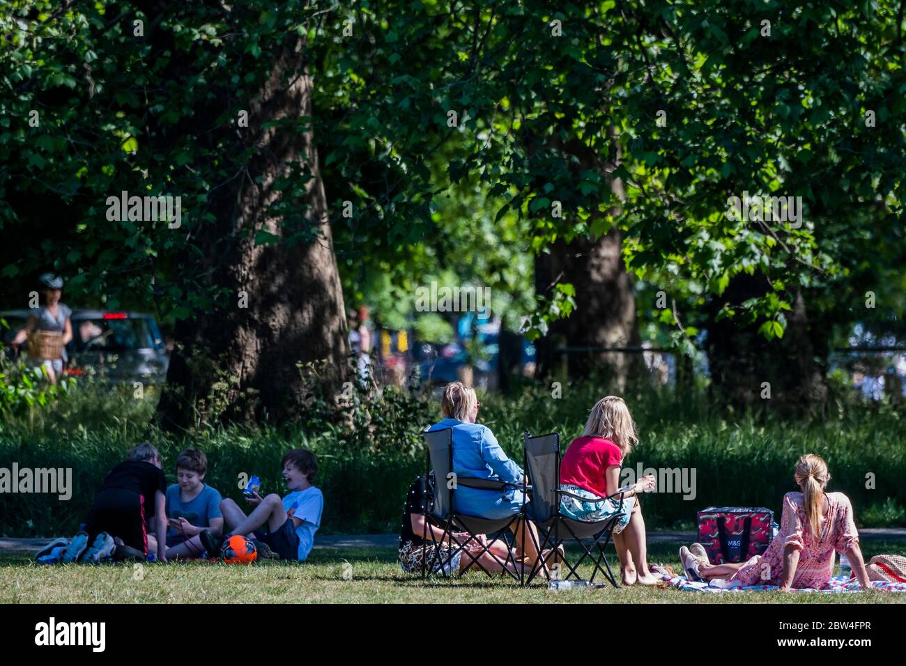 Londra, Regno Unito. 29 maggio 2020. Le madri cercano di raggiungere una distanza sociale lasciando che i loro figli giochino da vicino e condividano il cibo, Dimostrare confusione sulle regole - le persone godono del sole su Clapham Common dopo che il governo ha allentato le restrizioni e permesso alle persone di incontrarsi - Lambeth Consiglio hanno sostituito i segni per dire stare attenti e per permettere alle persone di sedersi sulle panchine. Il "blocco" dei morti continua per l'epidemia di Coronavirus (Covid 19) a Londra. Credit: Guy Bell/Alamy Live News Foto Stock