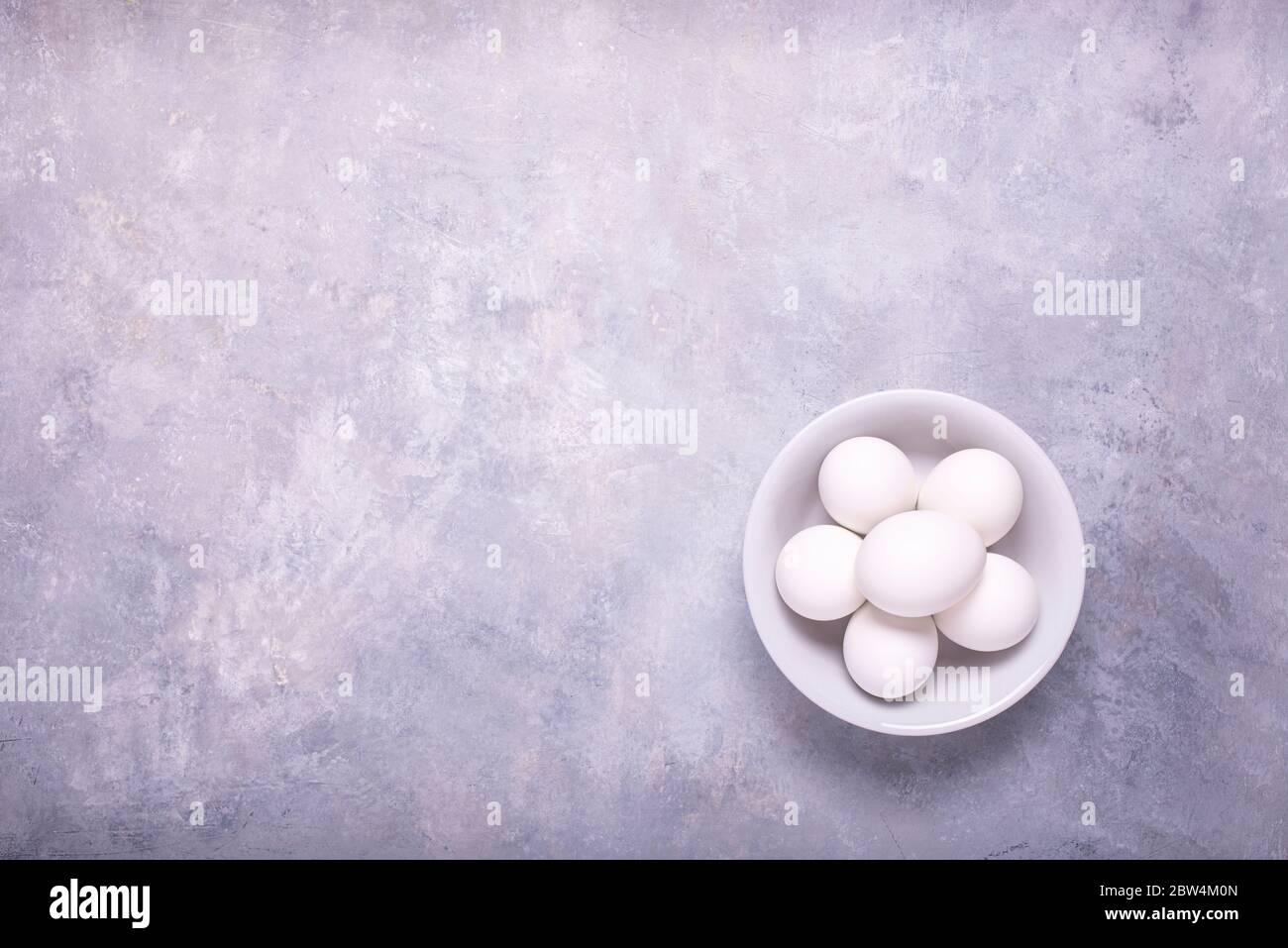 sullo sfondo grigio, con vista dall'alto, una ciotola isolata in ceramica con mezza dozzina di uova bianche per la preparazione di ricette culinarie Foto Stock
