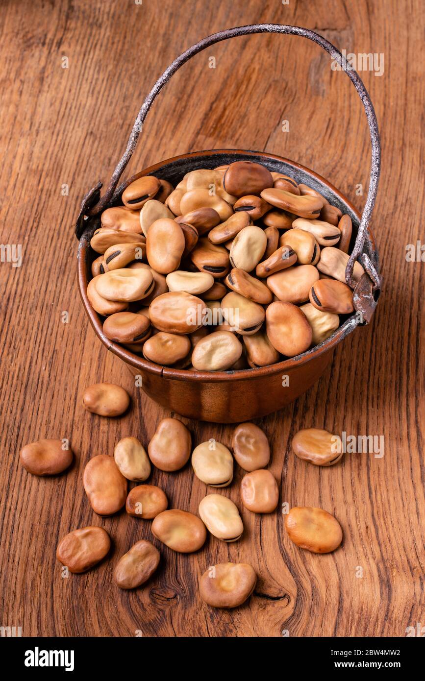 su sfondo di legno una padella di rame con fagioli secchi in primo piano Foto Stock