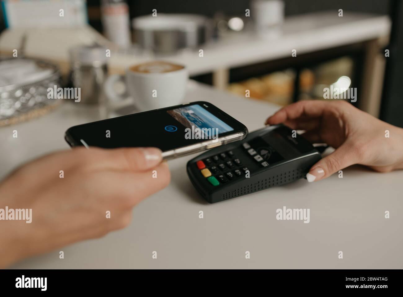 Una donna che paga il suo caffè con uno smartphone con la tecnologia SENZA contatto PAY PASS in un bar. Una barista femminile dispone di un terminale per pagare a un cl Foto Stock