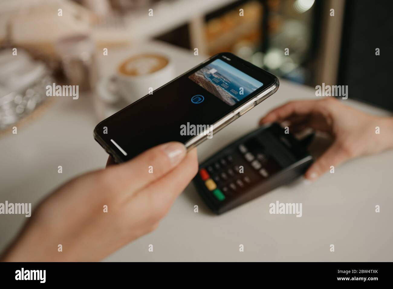Una donna che paga il suo latte con uno smartphone con la tecnologia SENZA contatto DI PAY PASS in un bar. Una barista femminile dispone di un terminale per pagare a un clie Foto Stock