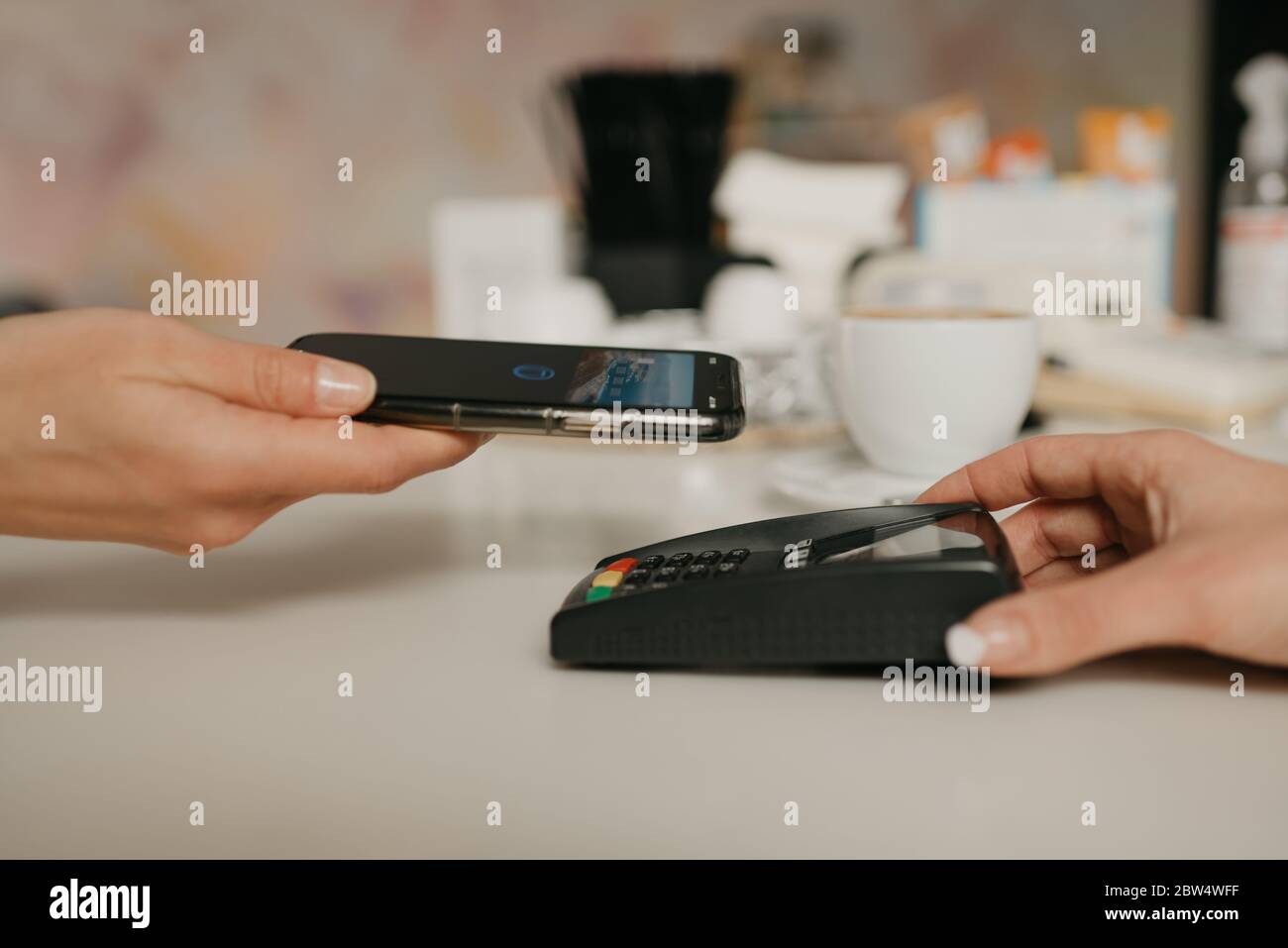 Una donna che si prepara a pagare per il latte con uno smartphone con tecnologia NFC senza contatto in un bar. Una barista femminile dispone di un terminale per pagare Foto Stock