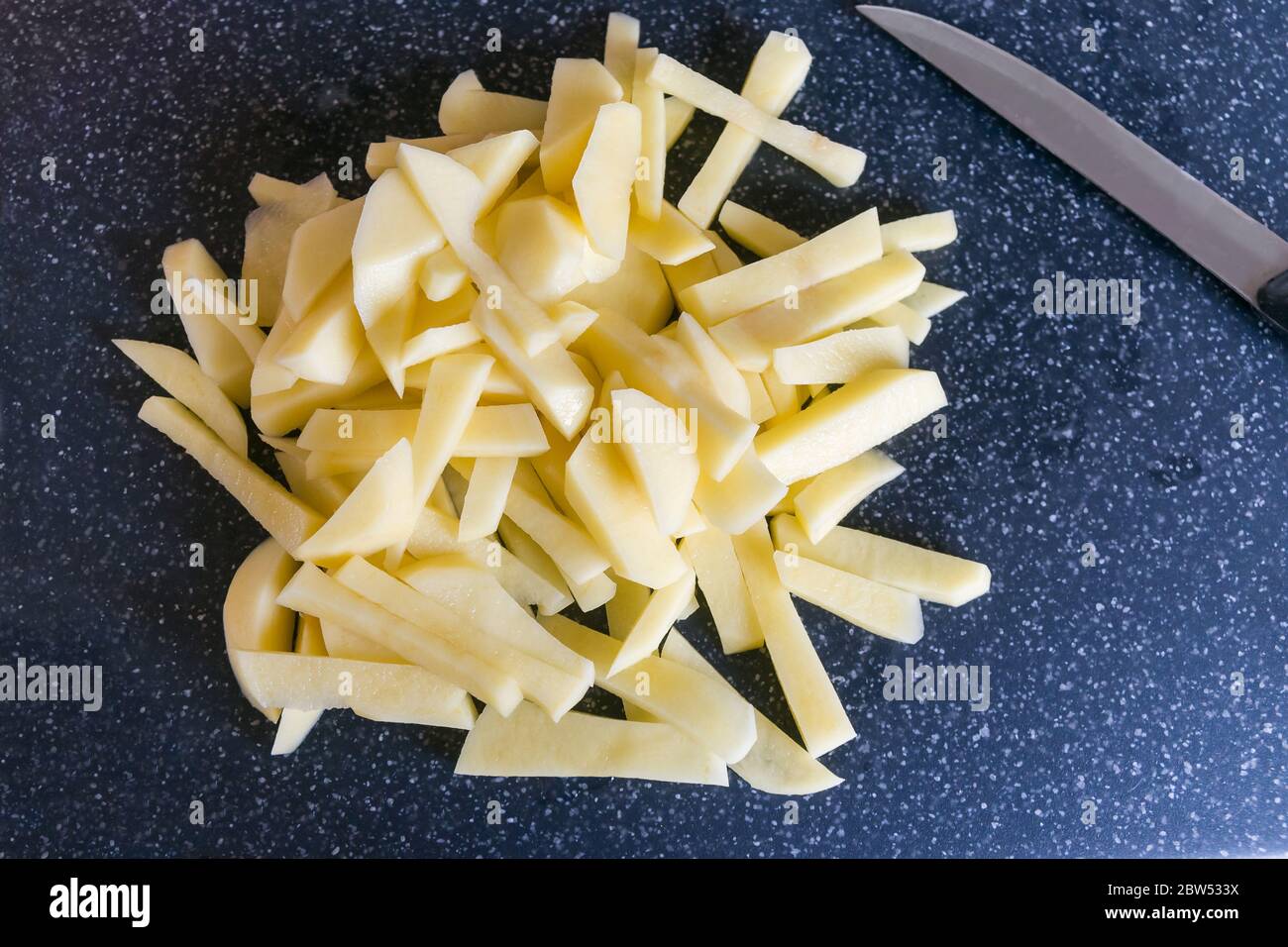 Patate fresche sbucciate e giulinate accanto a un coltello su un tagliere. Foto Stock