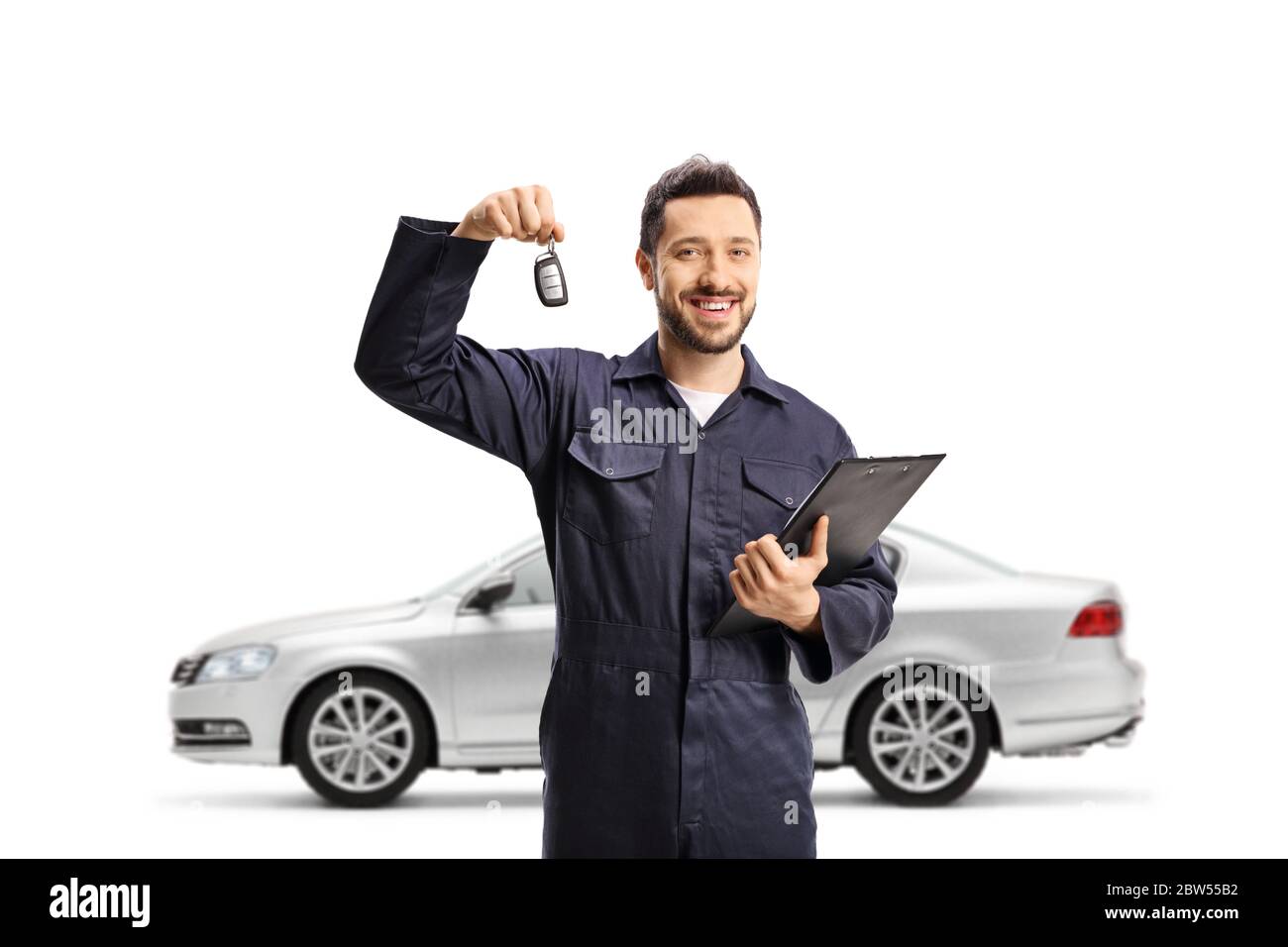 Meccanico automatico che tiene una clipboard con documenti e chiave di automobile e posa con un auto argentato isolato su sfondo bianco Foto Stock