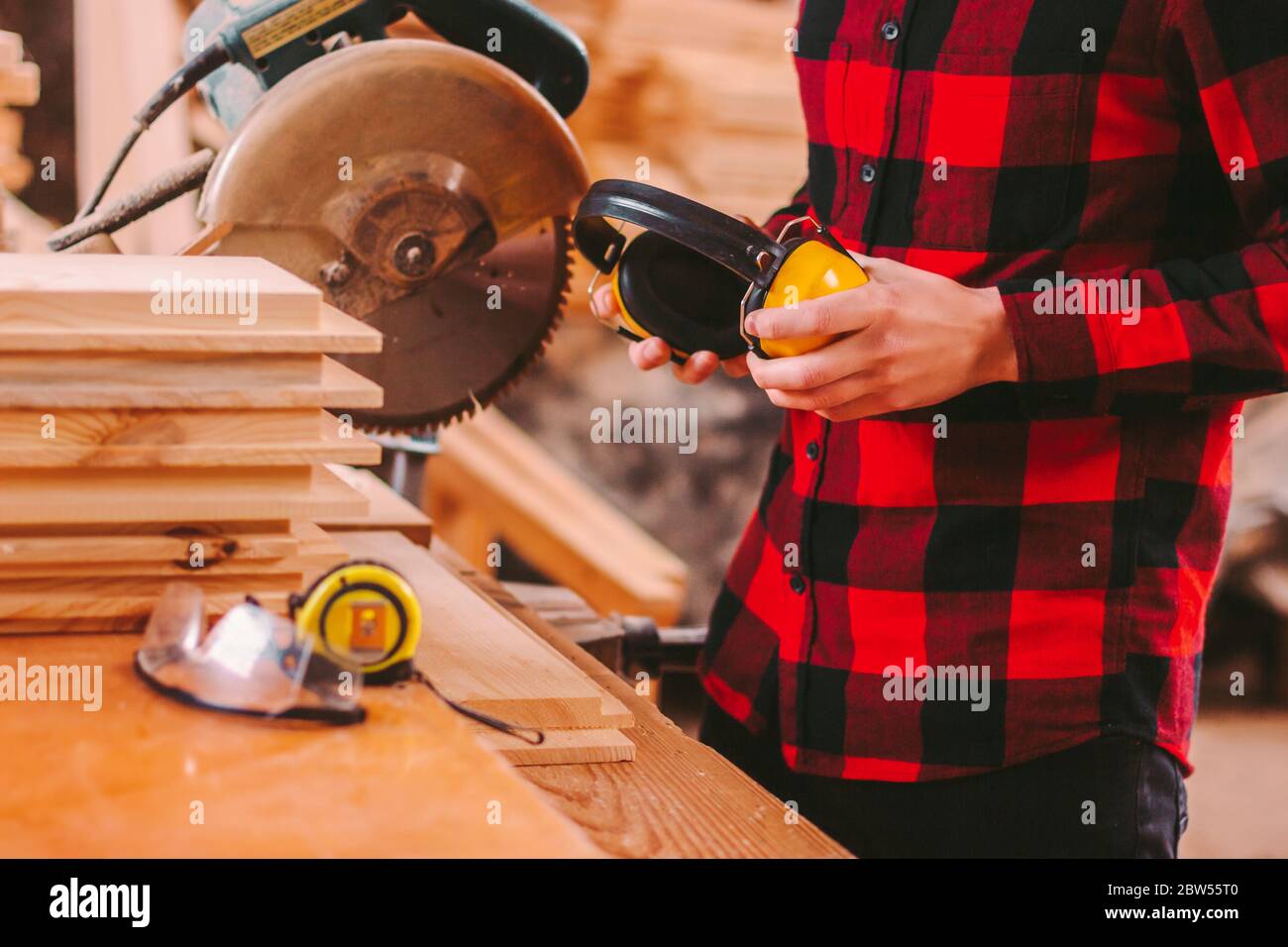 Guardaroba di un'azienda produttrice di armadietti professionale che tiene in mano le cuffie protettive gialle mentre lavora alla segheria. Lavoro di falegname specializzato per lavori in legno Foto Stock