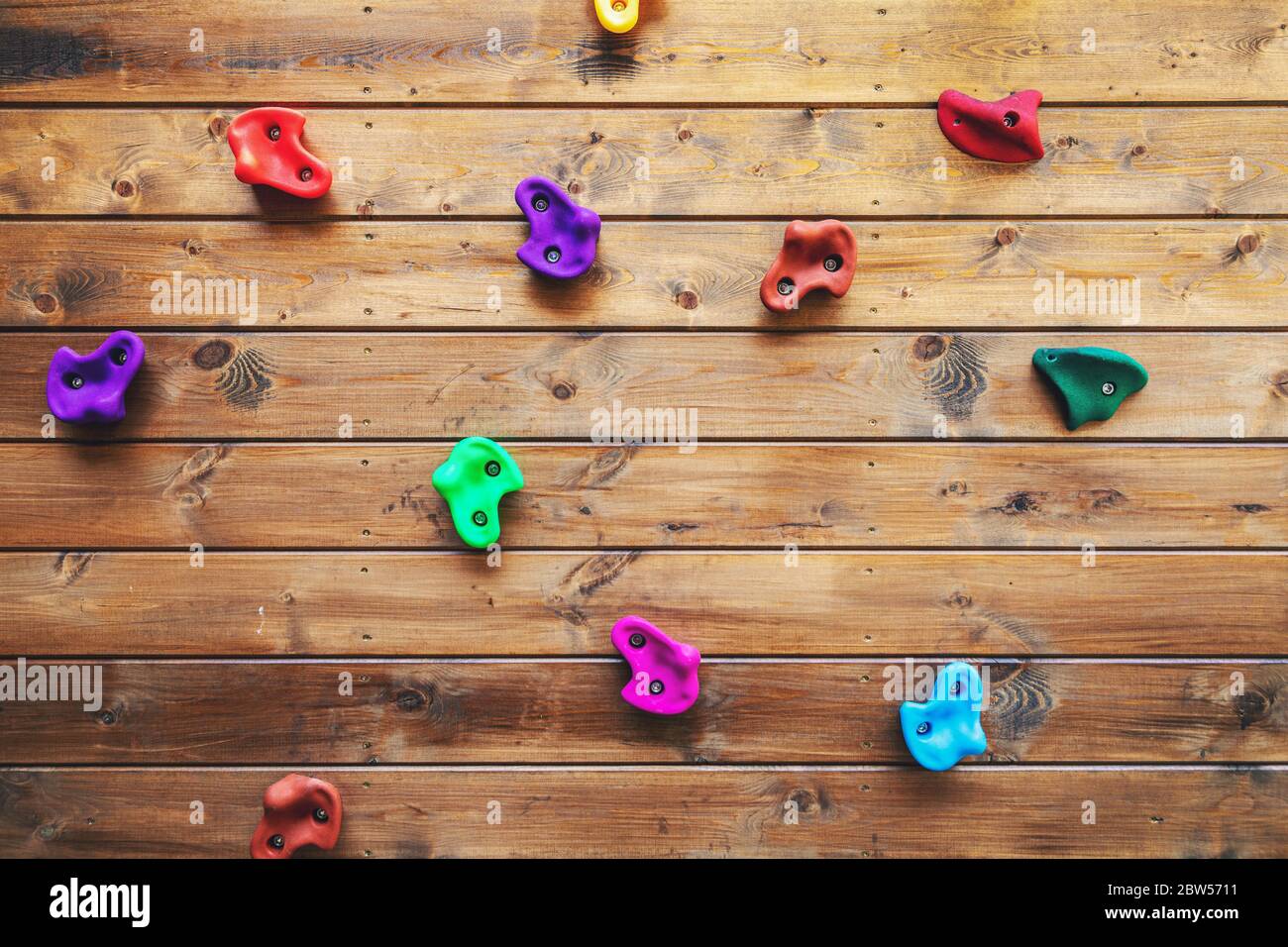 rocce colorate per arrampicata su parete per bambini su sfondo di legno nel parco giochi Foto Stock