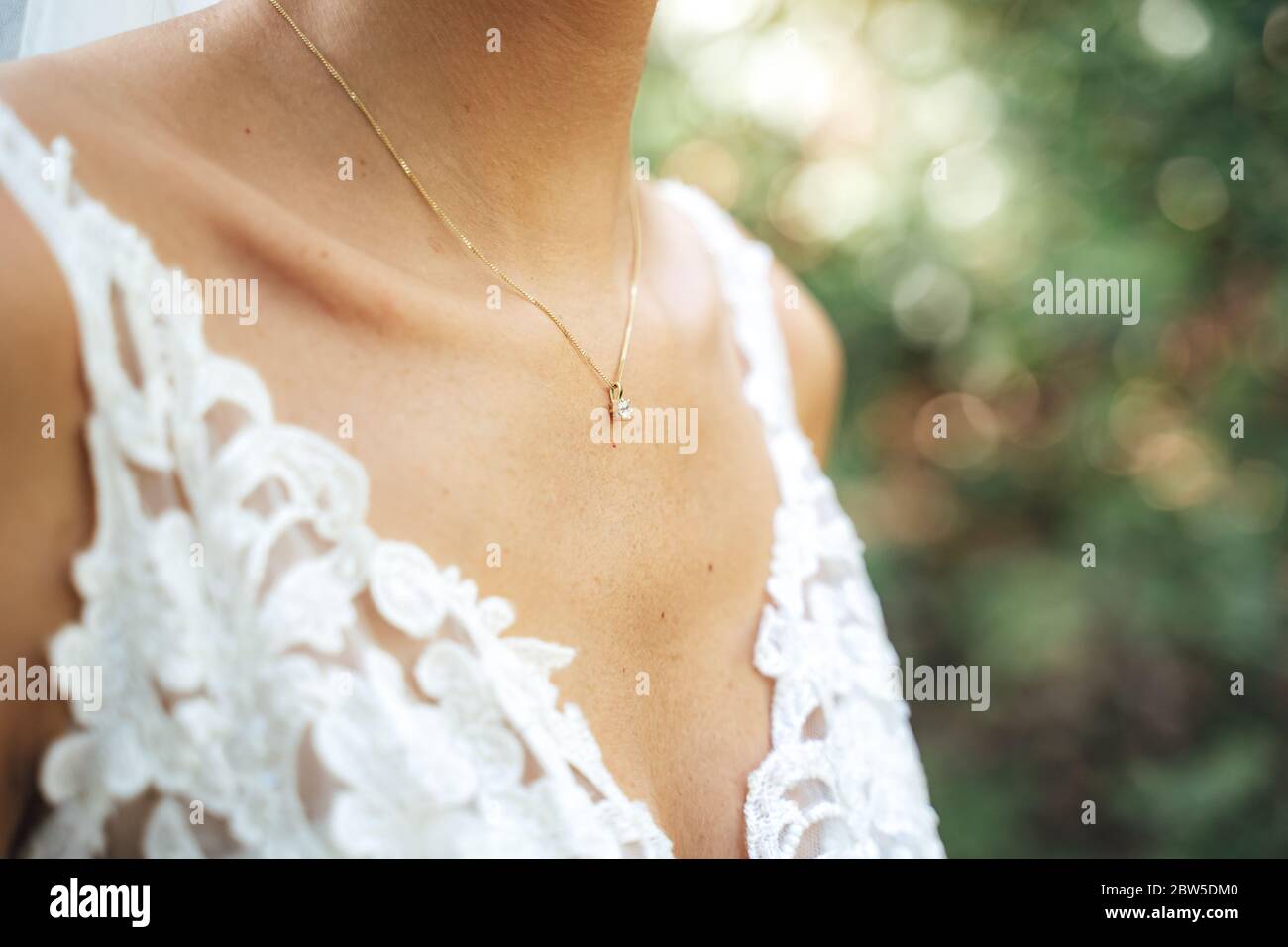 Primo piano del petto della sposa caucasica in abito da sposa in pizzo bianco. Collana decorata con collana dorata con gemme. Concetto di giorno di nozze. Foto Stock