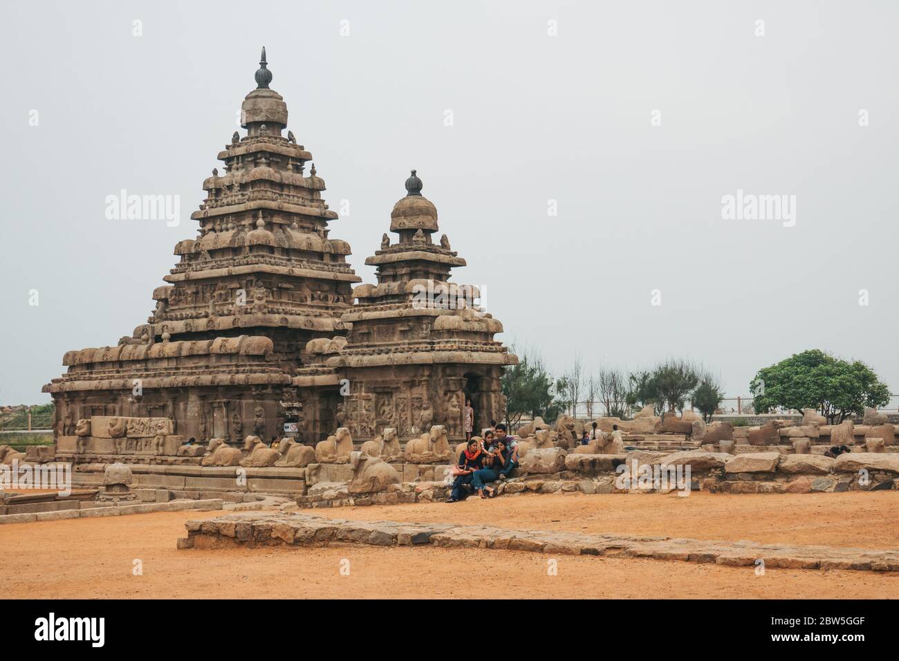 I turisti si rilassano al Tempio Shore, uno dei più antichi templi indù strutturali dell'India a Mahabalipuram, Tamil Nadu Foto Stock