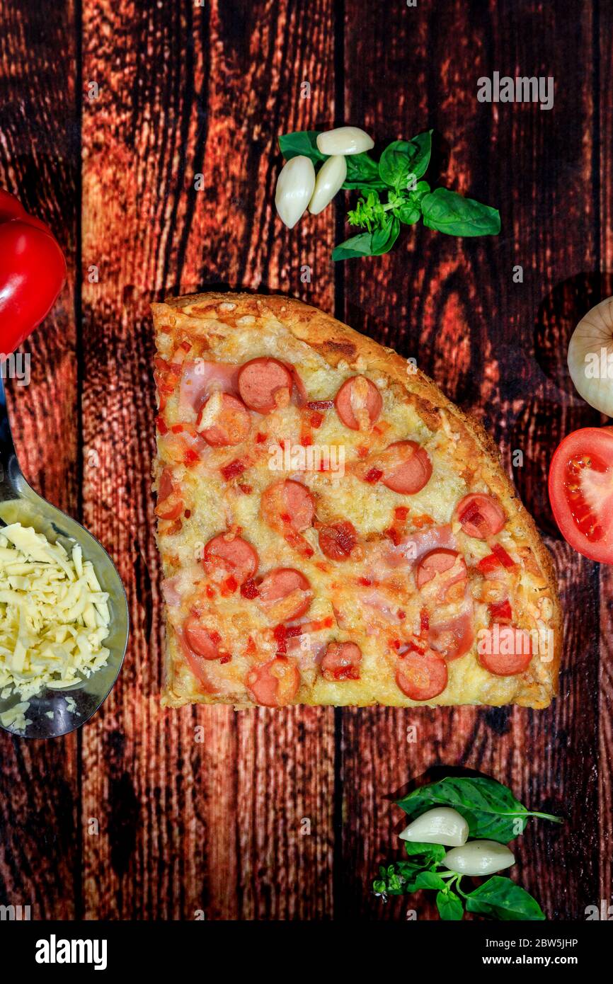Vista dall'alto di salsiccia, prosciutto, pepe e pizza al formaggio su sfondo scuro in legno con pezzi di ingredienti freschi Foto Stock