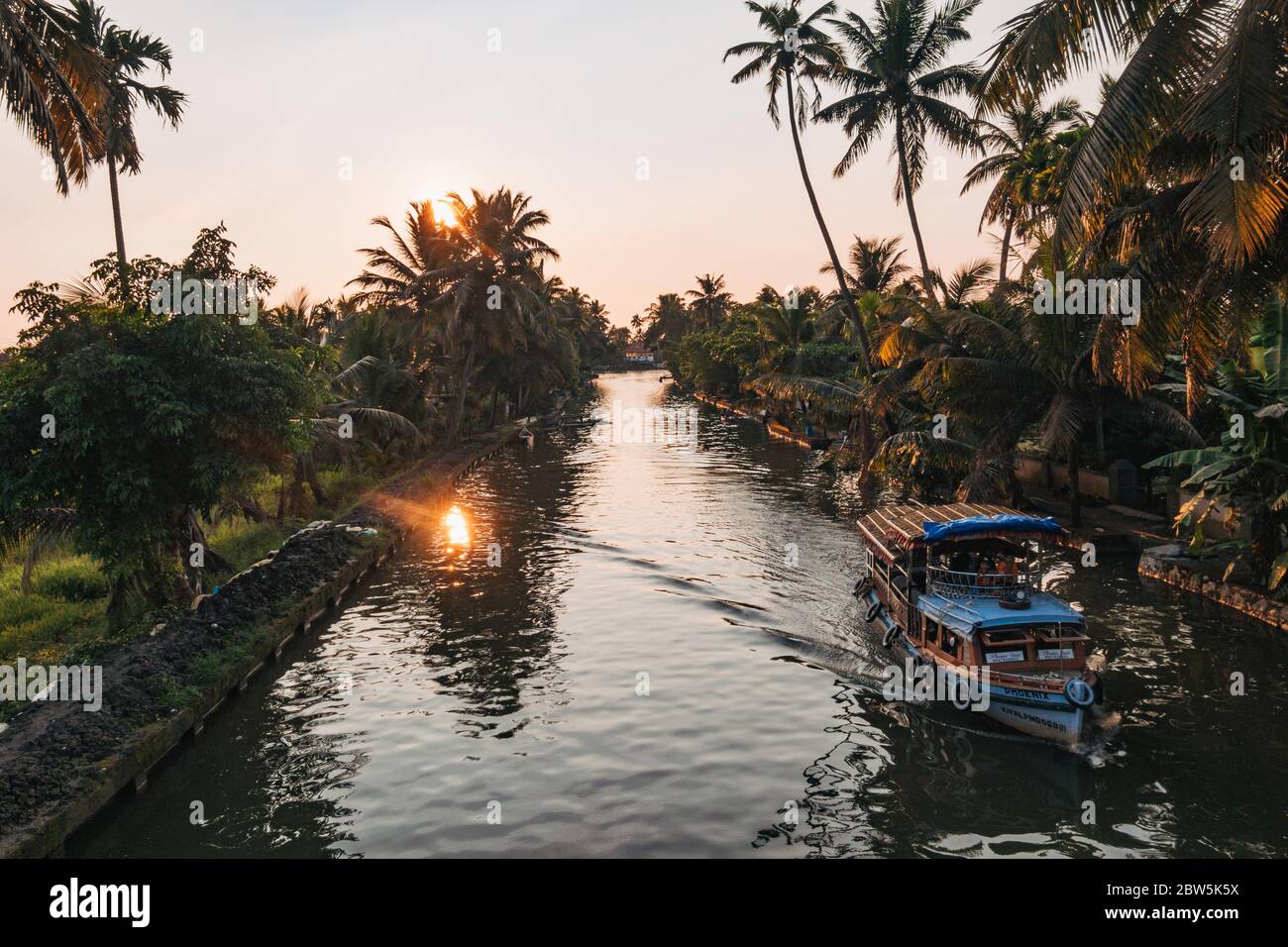 Una casa galleggiante naviga lungo un canale nel Kerala backwaters al sole di sera Foto Stock