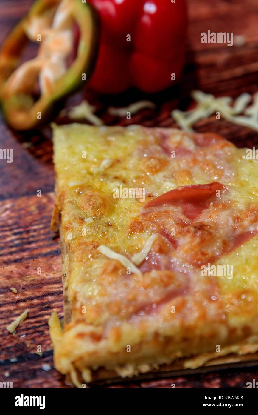 A metà fetta di pizza con prosciutto, salame e formaggio su fondo di legno con ingredienti freschi sulla parte superiore Foto Stock