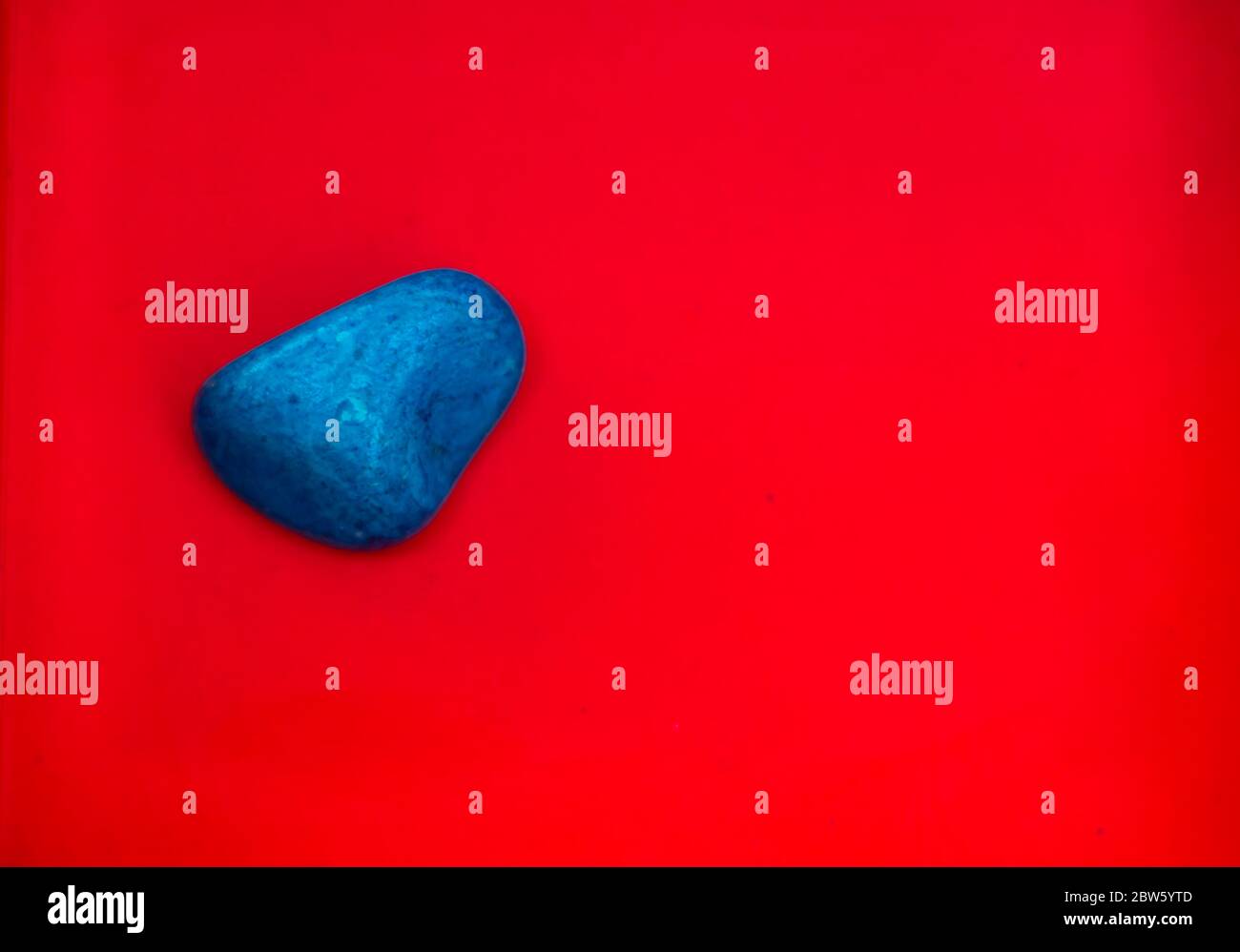 Colore blu Pebbles naturali isolati su sfondo rosso con spazio per copiare testo e parole. Pietra naturale multicolore. Pietra di colore blu isolata Foto Stock