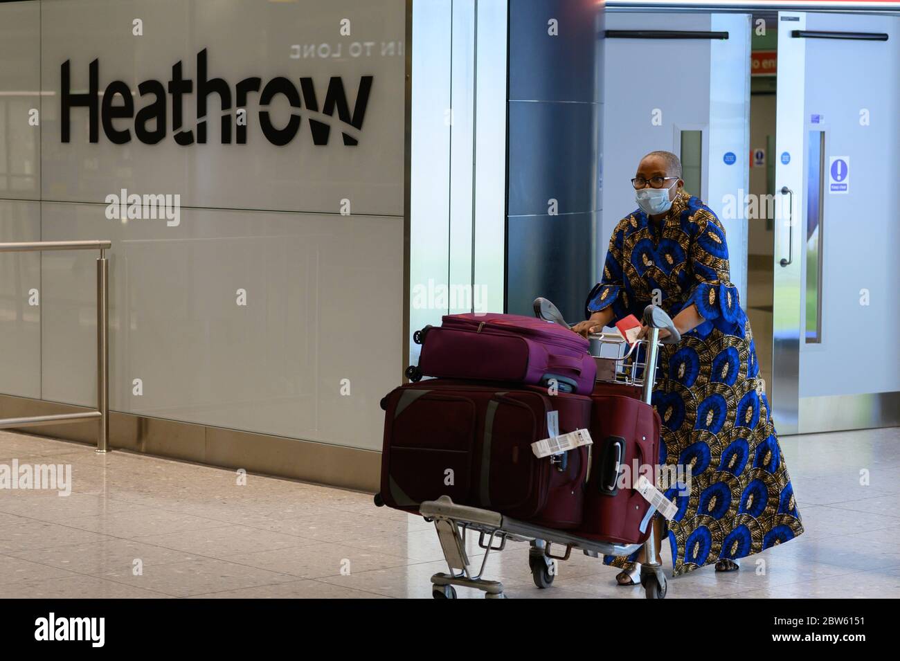 Donna britannica nera con stampa in cera africana, con bagaglio a spinta, arriva al terminal 2 di Heathrow da Lagos, Nigeria Foto Stock