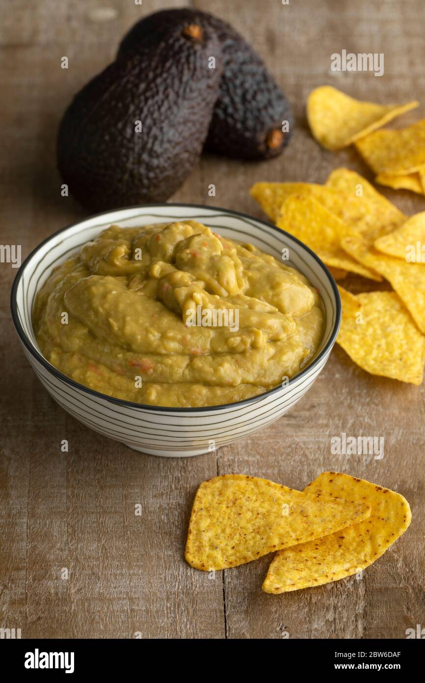 Guacamole fresche fatte in casa con patatine di tortilla e avocado sullo sfondo di un tavolo di legno Foto Stock