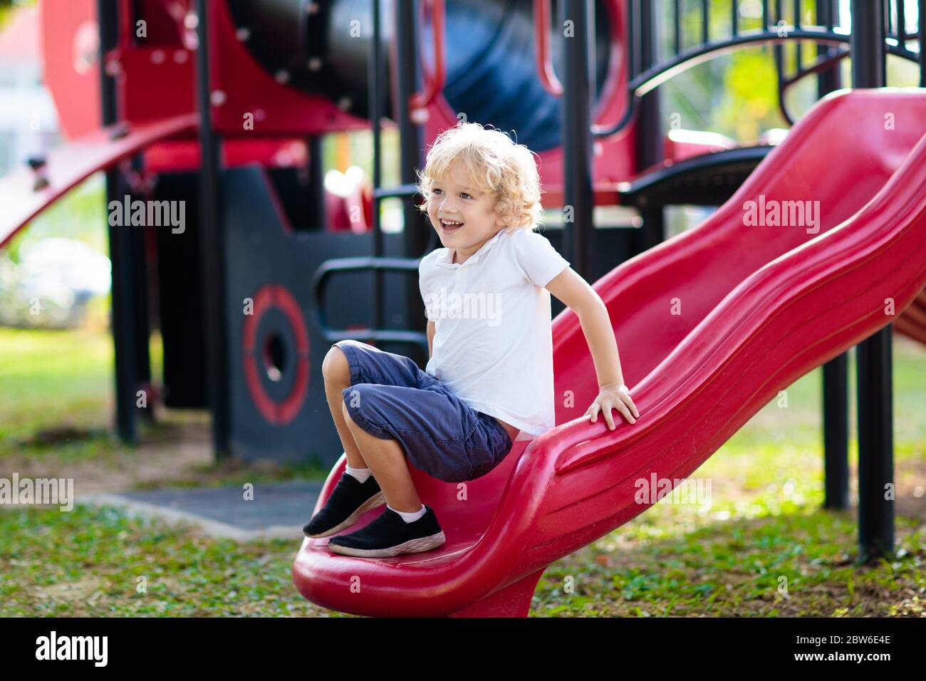 Bambino che gioca sul parco giochi all'aperto. Bambini a giocare sulla scuola o asilo nido cantiere. Capretto attivo sulla colorata scivolo e altalena. Una sana attività estiva per chi Foto Stock