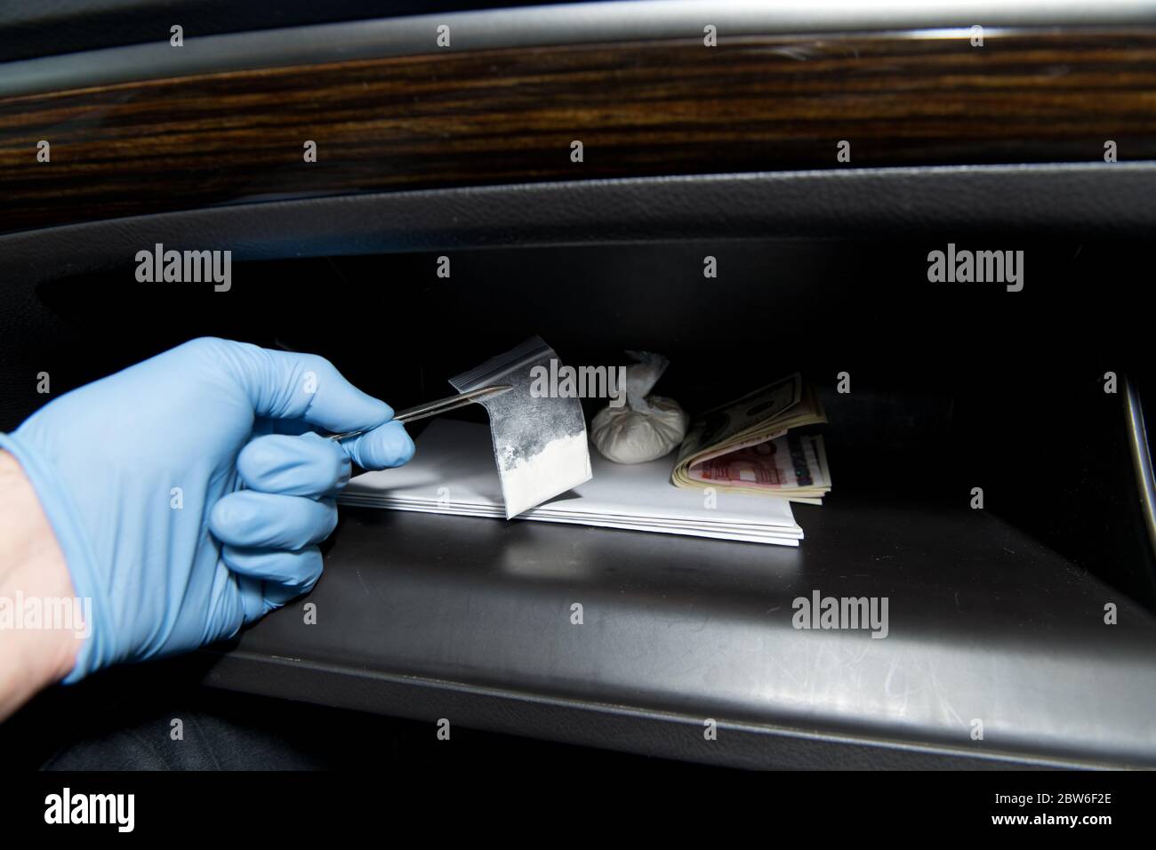 una mano guanto toglie la cocaina delle pinzette dal vano portaoggetti di un'auto. Foto Stock