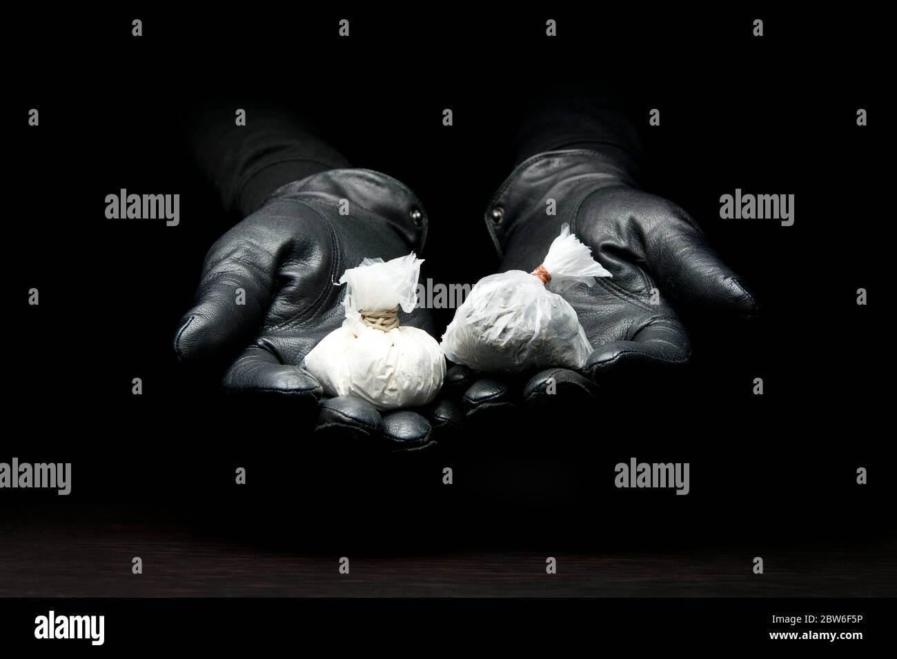 mani in guanti dal buio tenere fuori una borsa di polvere e una borsa di hash di vostra scelta Foto Stock