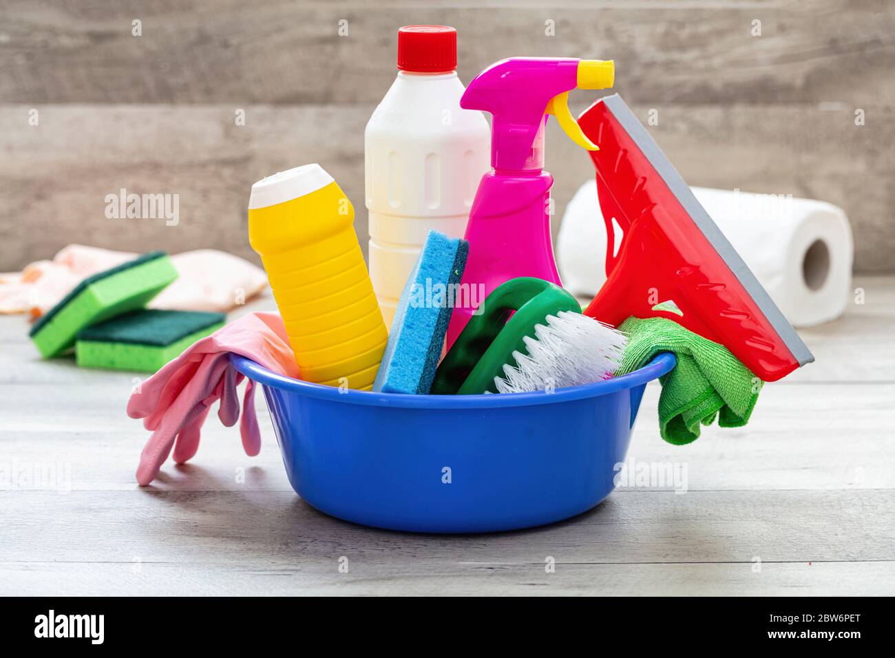 Prodotti per la pulizia sul pavimento, sfondo interno casa. Bottiglie di detergente chimico in un recipiente blu. Pulizia sanitaria domestica o aziendale Foto Stock