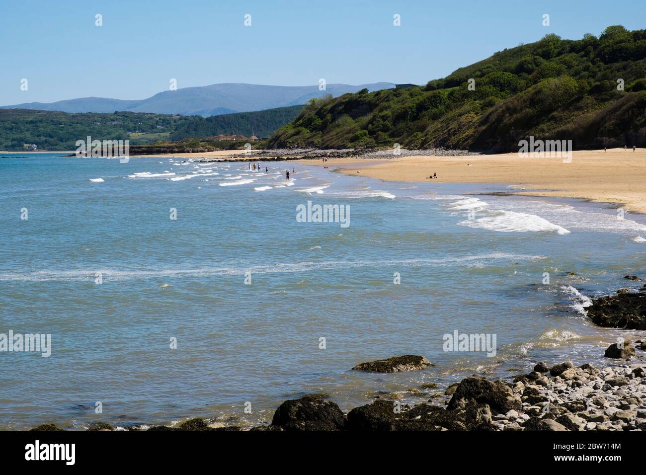 Alcune persone socialmente distanziando in mare su spiaggia tranquilla durante il COVID-19 blocco pandemico a mezza vacanza. Bennlech Anglesey Wales Gran Bretagna Foto Stock