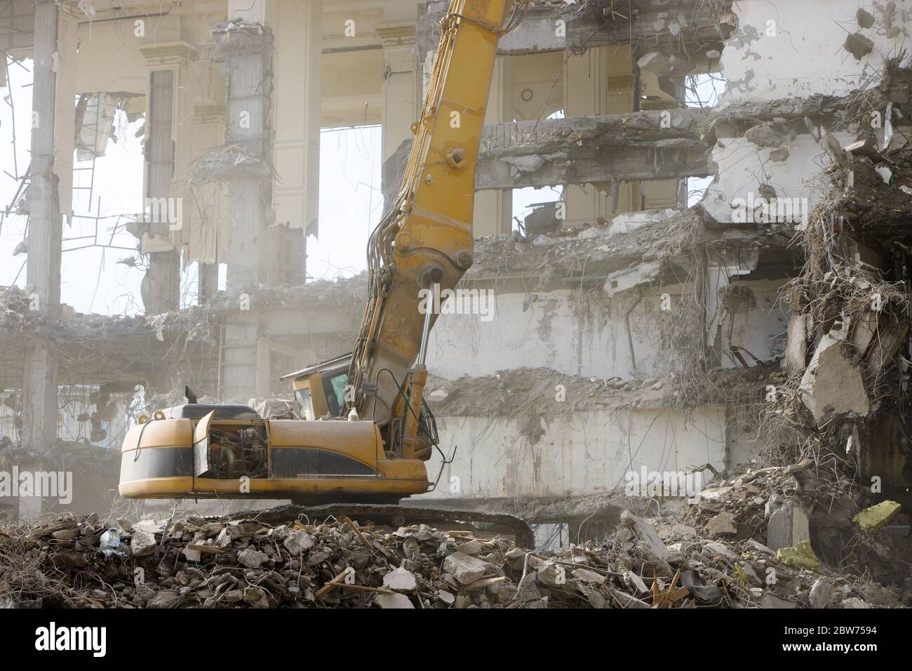 Primo piano di un escavatore idraulico-distruttore speciale durante il funzionamento, polvere di calcestruzzo nell'aria, rovine di un edificio sullo sfondo. Demolizione ultra elevata Foto Stock