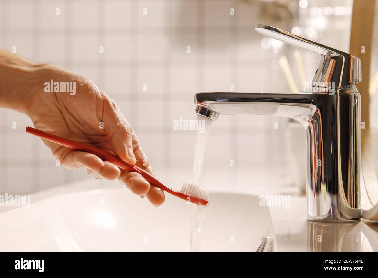 Uomo che pulisce la spazzola del dente sotto l'acqua corrente in bagno, pulendola, fuoco morbido. Procedure di coricarsi, igiene orale/dentista. Foto Stock