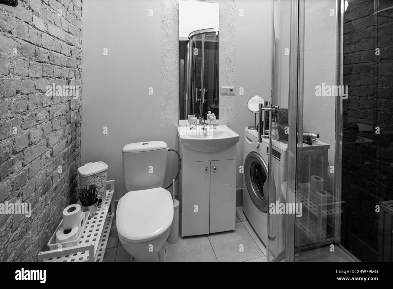 Interno soppalco del bagno in appartamento. Cabina doccia. Lavatrice. Lavabo bianco con specchio. WC. Muro di mattoni. Foto Stock