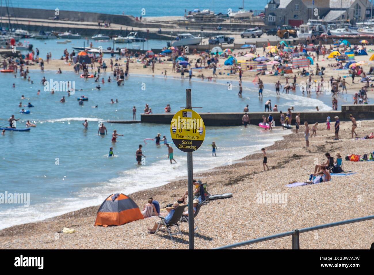 Lyme Regis, Dorset, Regno Unito. 30 maggio 2020. Regno Unito Meteo. Social distancing segni promemoria a Lyme Regis dove i beachgoers e le famiglie hanno imballato la spiaggia questo pomeriggio per crogiolarsi nel caldo sole del pomeriggio il giorno più caldo dell'anno. Credit: Celia McMahon/Alamy Live News. Foto Stock
