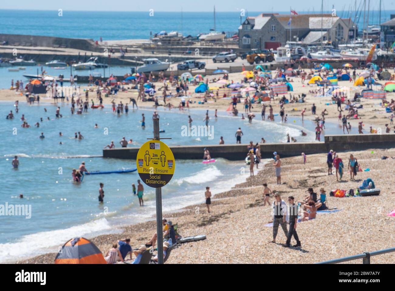 Lyme Regis, Dorset, Regno Unito. 30 maggio 2020. Regno Unito Meteo. Social distancing segni promemoria a Lyme Regis dove i beachgoers e le famiglie hanno imballato la spiaggia questo pomeriggio per crogiolarsi nel caldo sole del pomeriggio il giorno più caldo dell'anno. Credit: Celia McMahon/Alamy Live News. Foto Stock