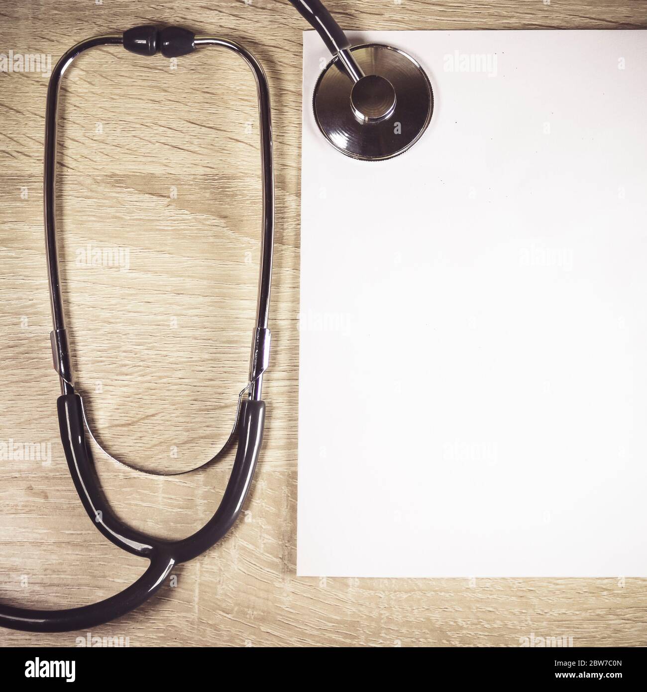 Uno stetoscopio e un foglio bianco di carta su sfondo di legno. Un luogo in cui inserire il testo. Primo piano. Foto Stock