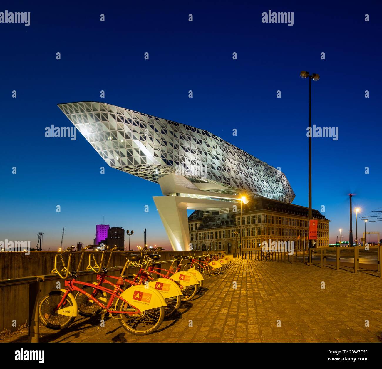 La Port House di Anversa di notte con una linea di City Bike (Antwerp Velo) Foto Stock